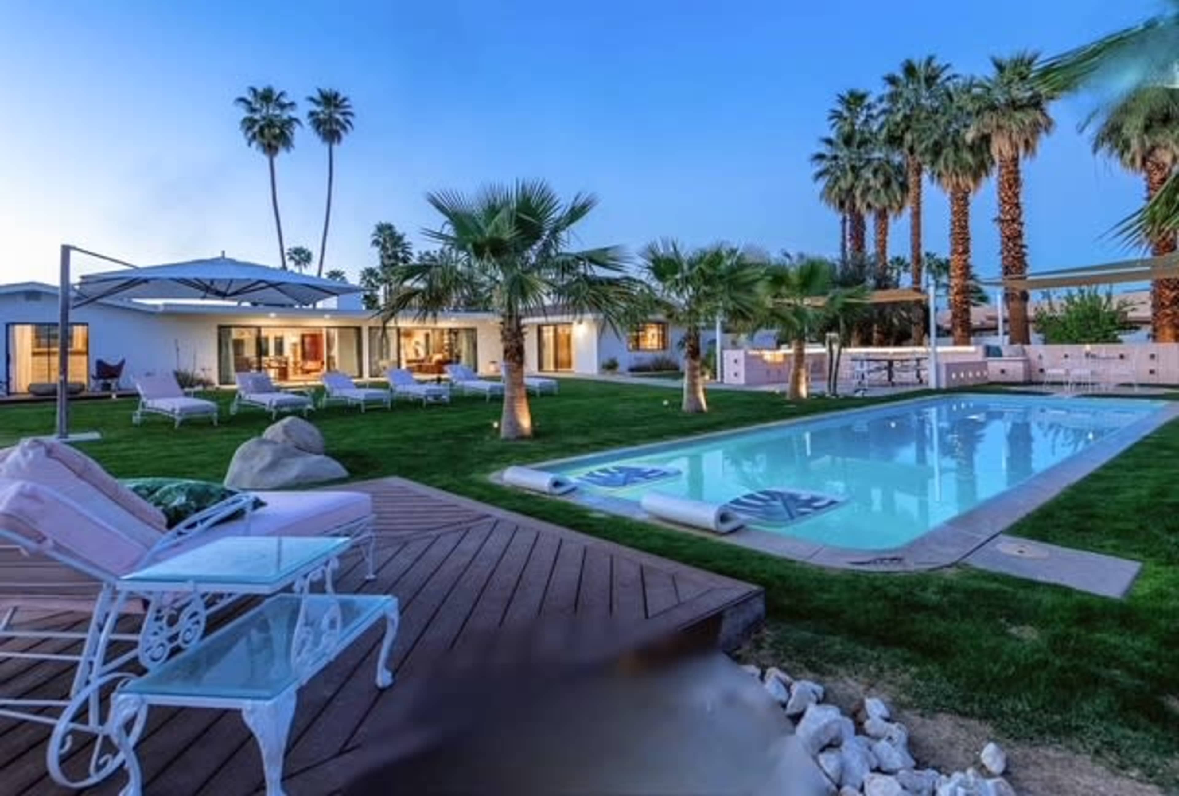 The image shows a spacious backyard with a pool, palm trees, and lounge chairs, surrounded by a modern house.