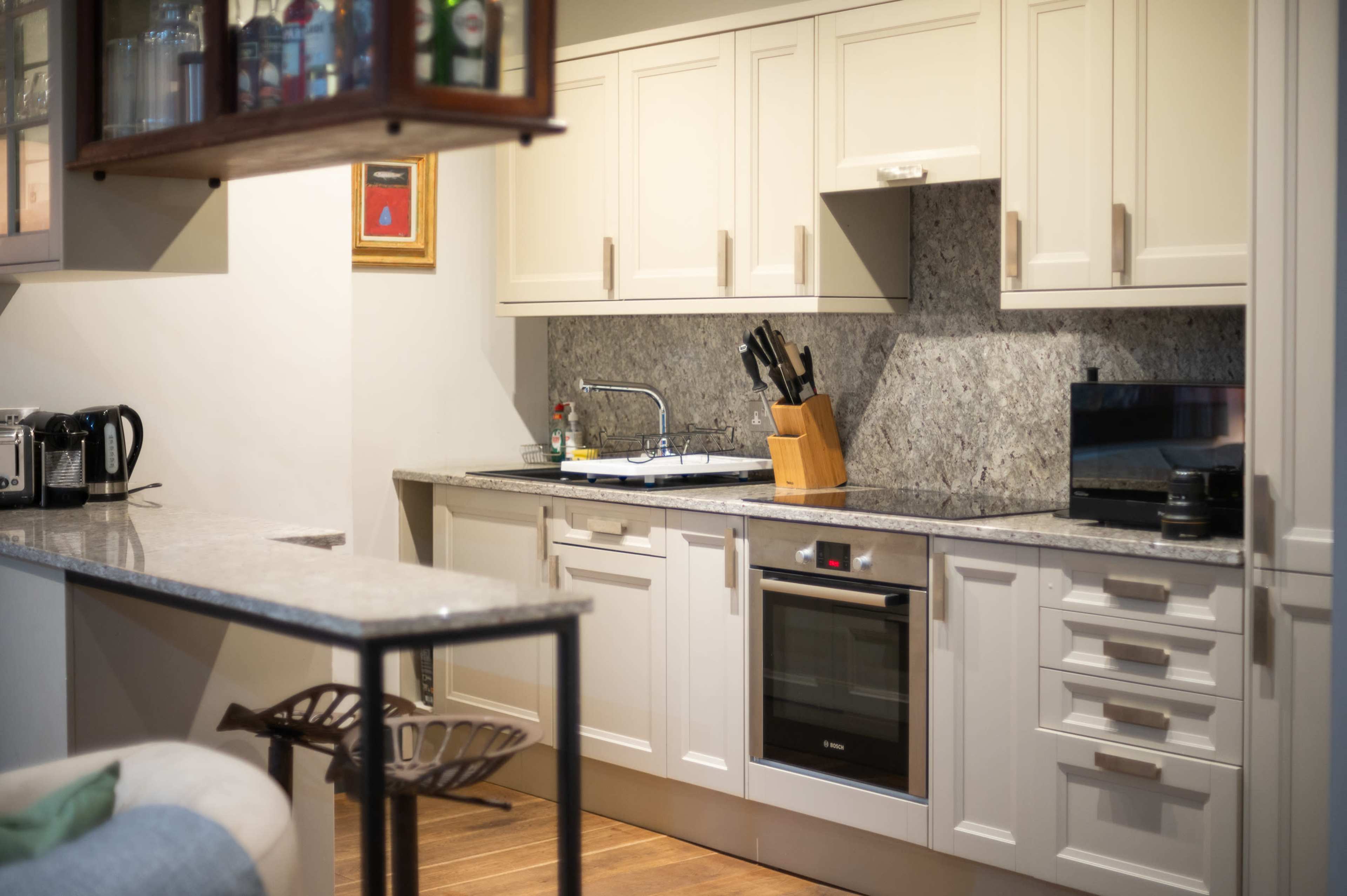 The image shows a modern kitchen with cream-colored cabinets, a marble countertop, and stainless steel appliances.