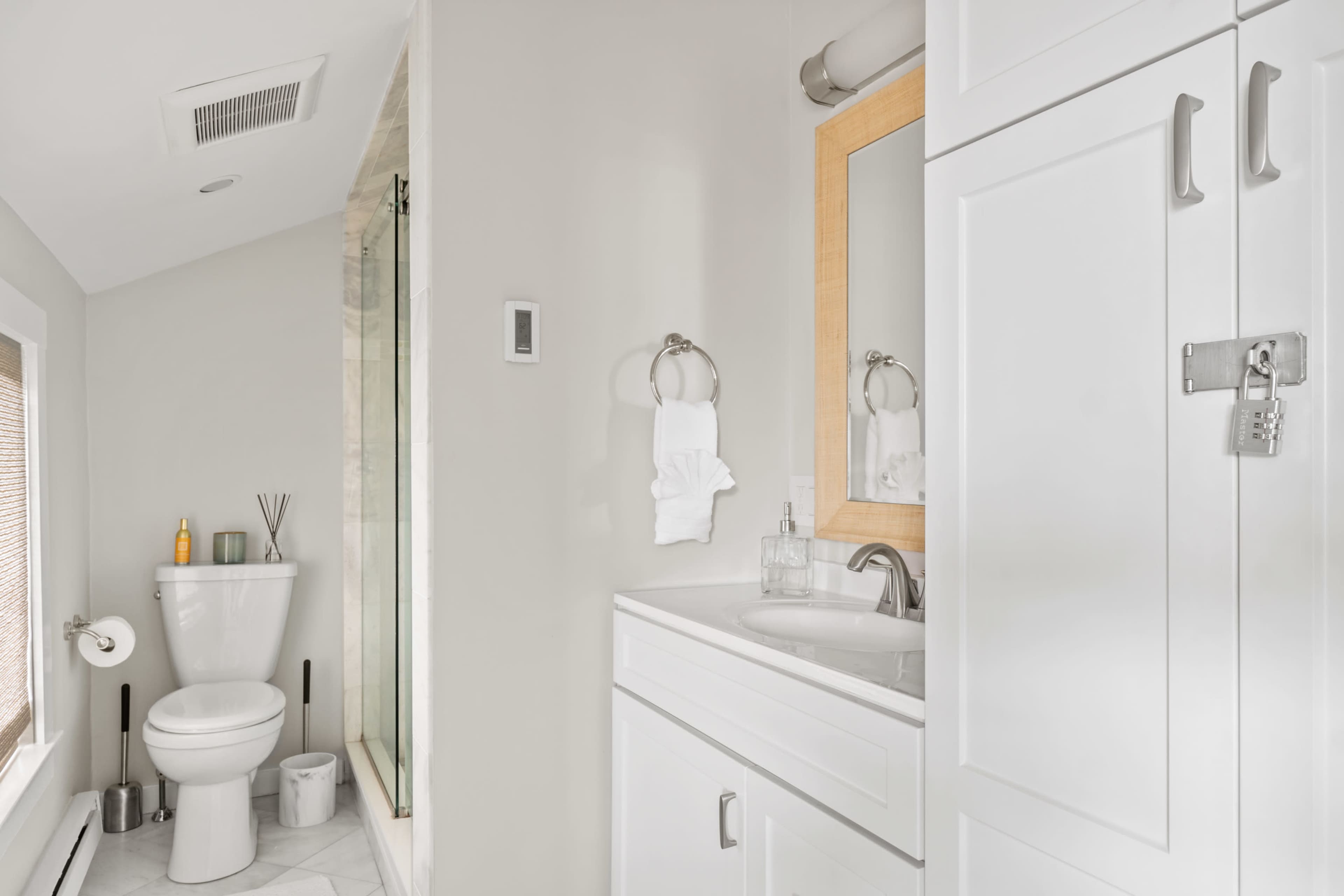 A modern bathroom featuring a shower, a toilet, a sink with a mirror, and cabinetry against a light-colored wall.
