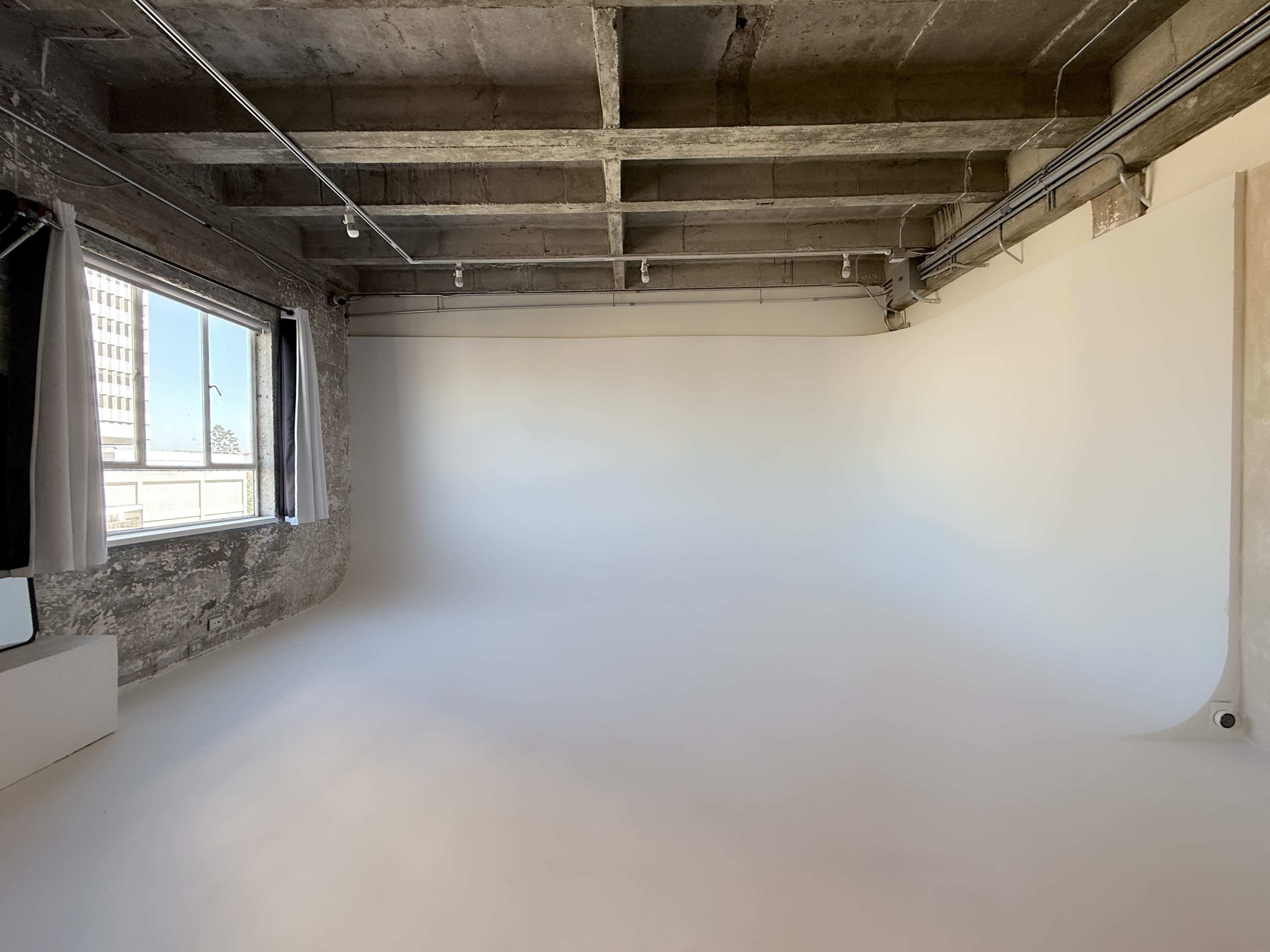 The image shows a spacious photography studio with a seamless white backdrop and large windows allowing natural light to enter.