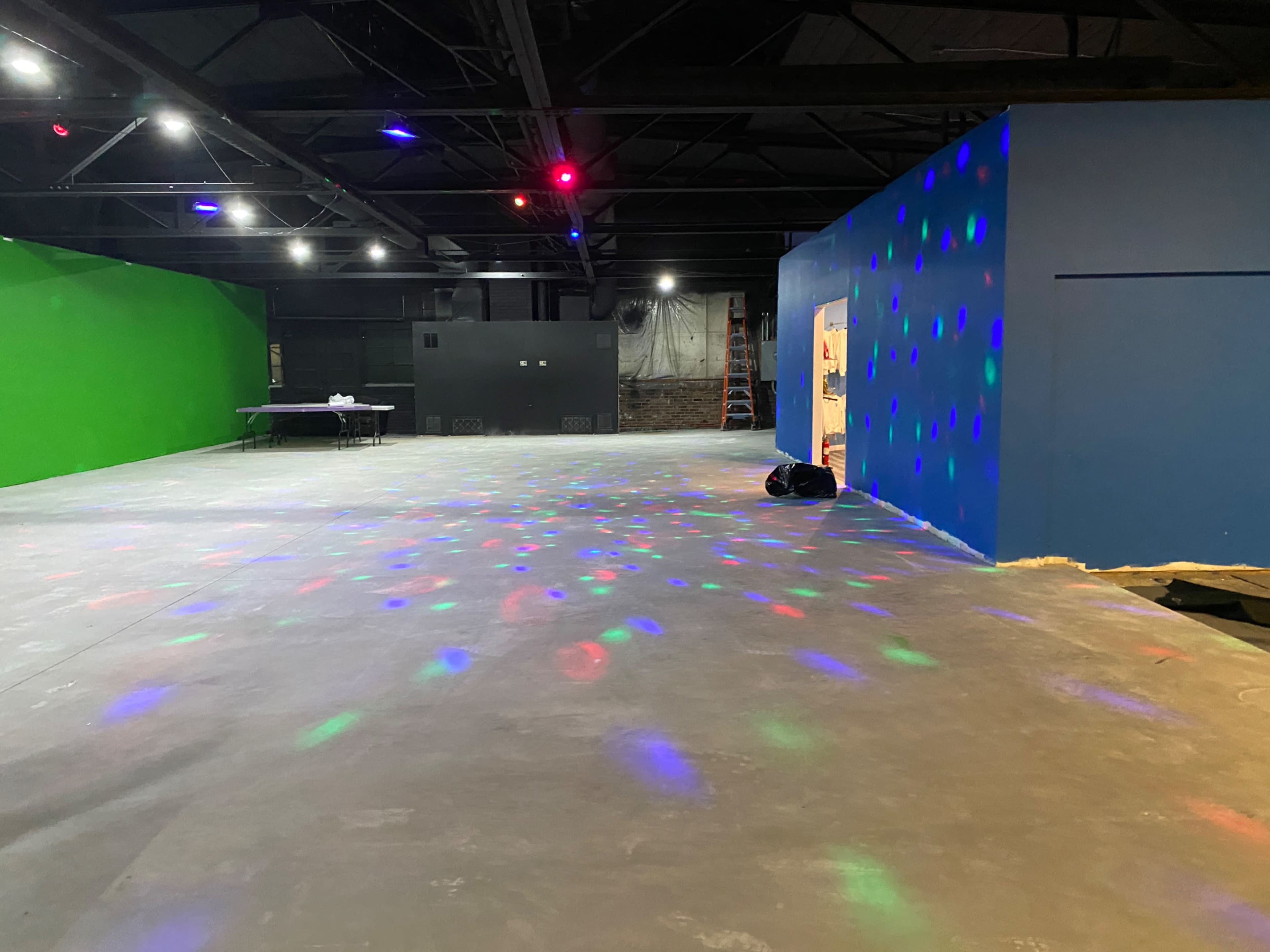 The image shows a spacious interior with green and blue walls, a concrete floor, and colorful lights projecting patterns on the surface.