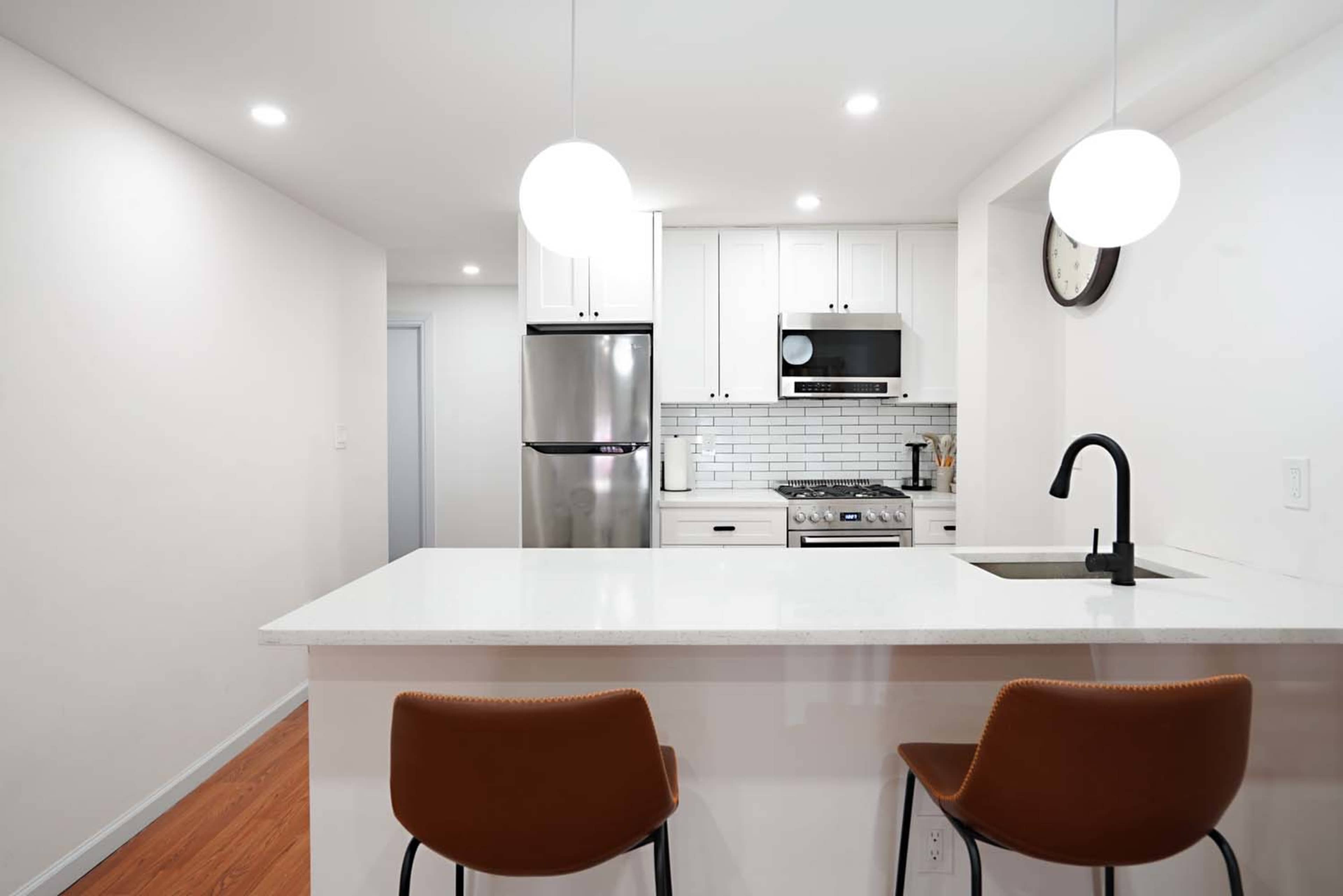 A modern kitchen features white cabinetry, stainless steel appliances, and a central island with two brown bar stools.