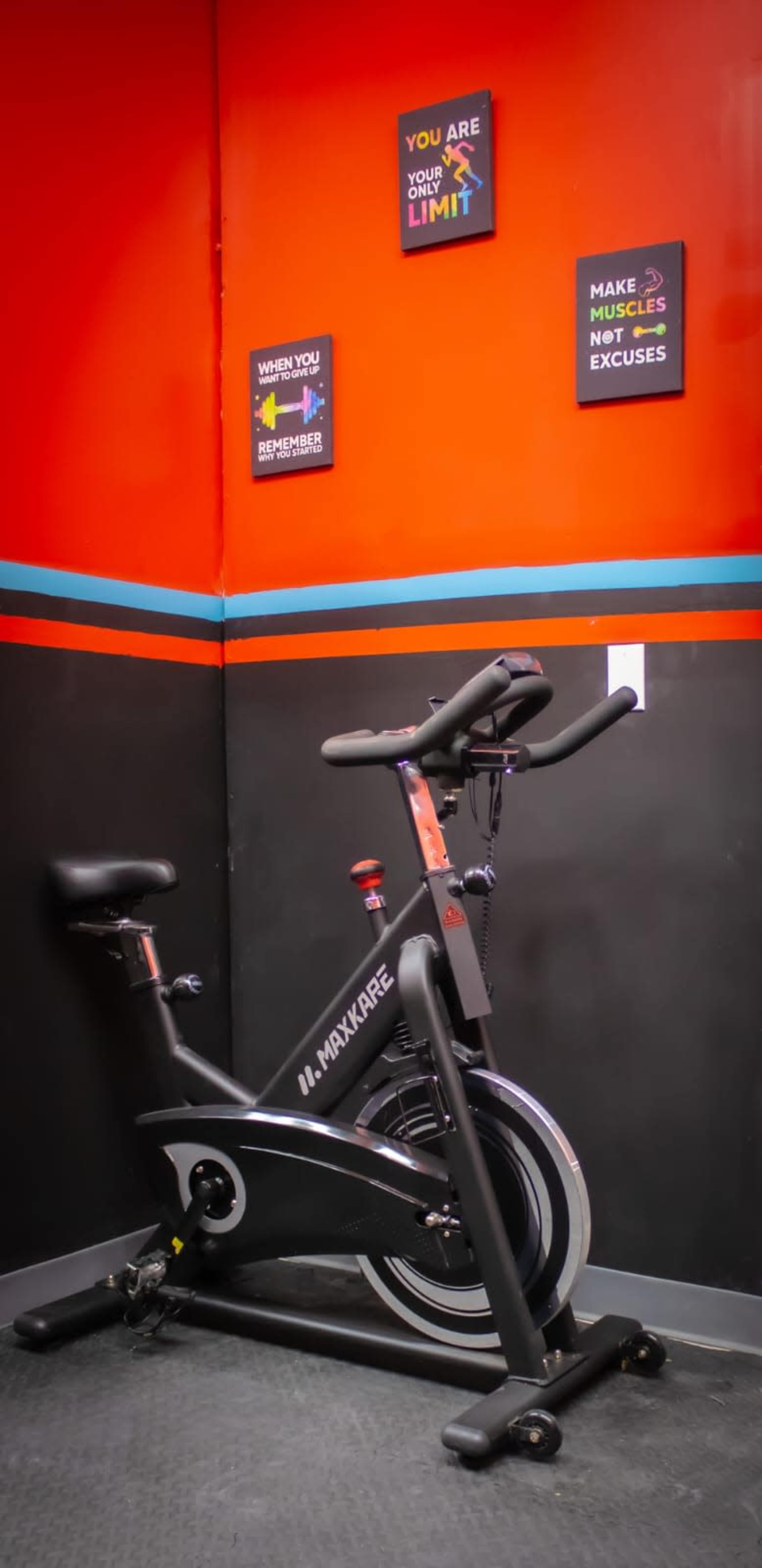 A stationary exercise bike is positioned against a bright red wall, accompanied by motivational posters.