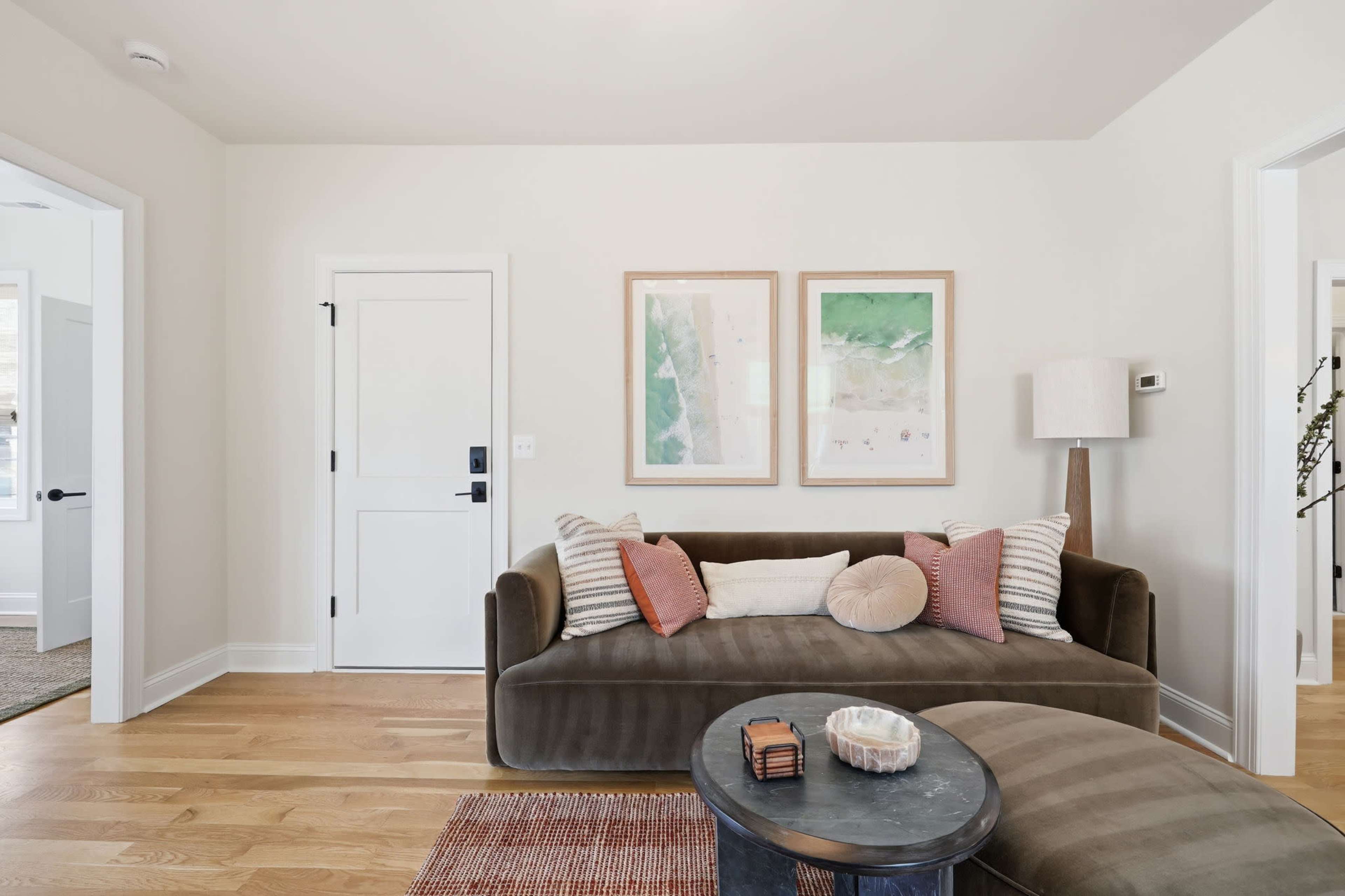 The image shows a modern living room with a dark green sofa adorned with decorative pillows, a round coffee table, and framed artwork on the walls.