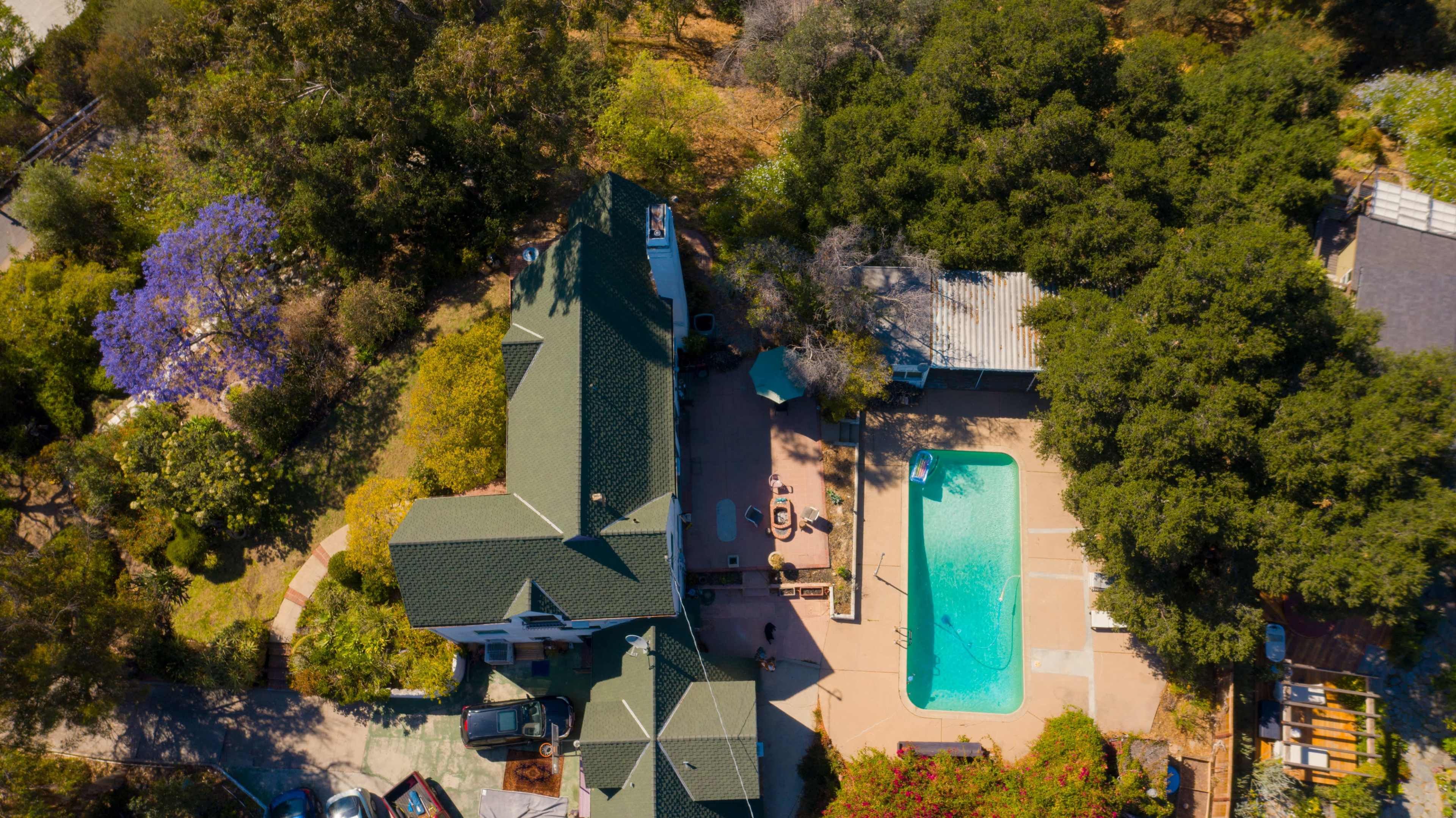 An aerial view of a house with a swimming pool surrounded by trees and patio furniture.