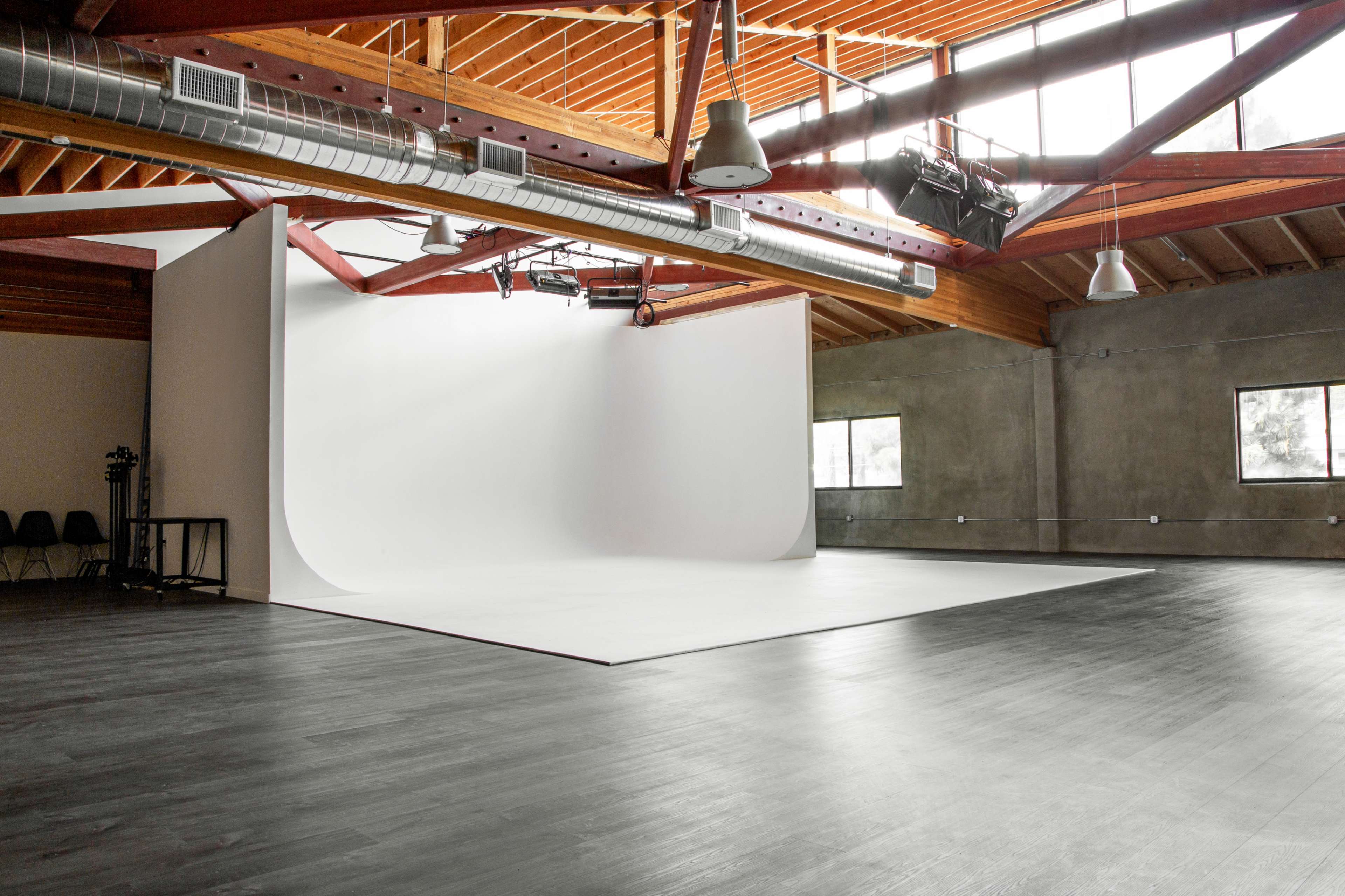 A spacious photography studio with a seamless white backdrop, high wooden ceilings, and large windows allowing natural light.