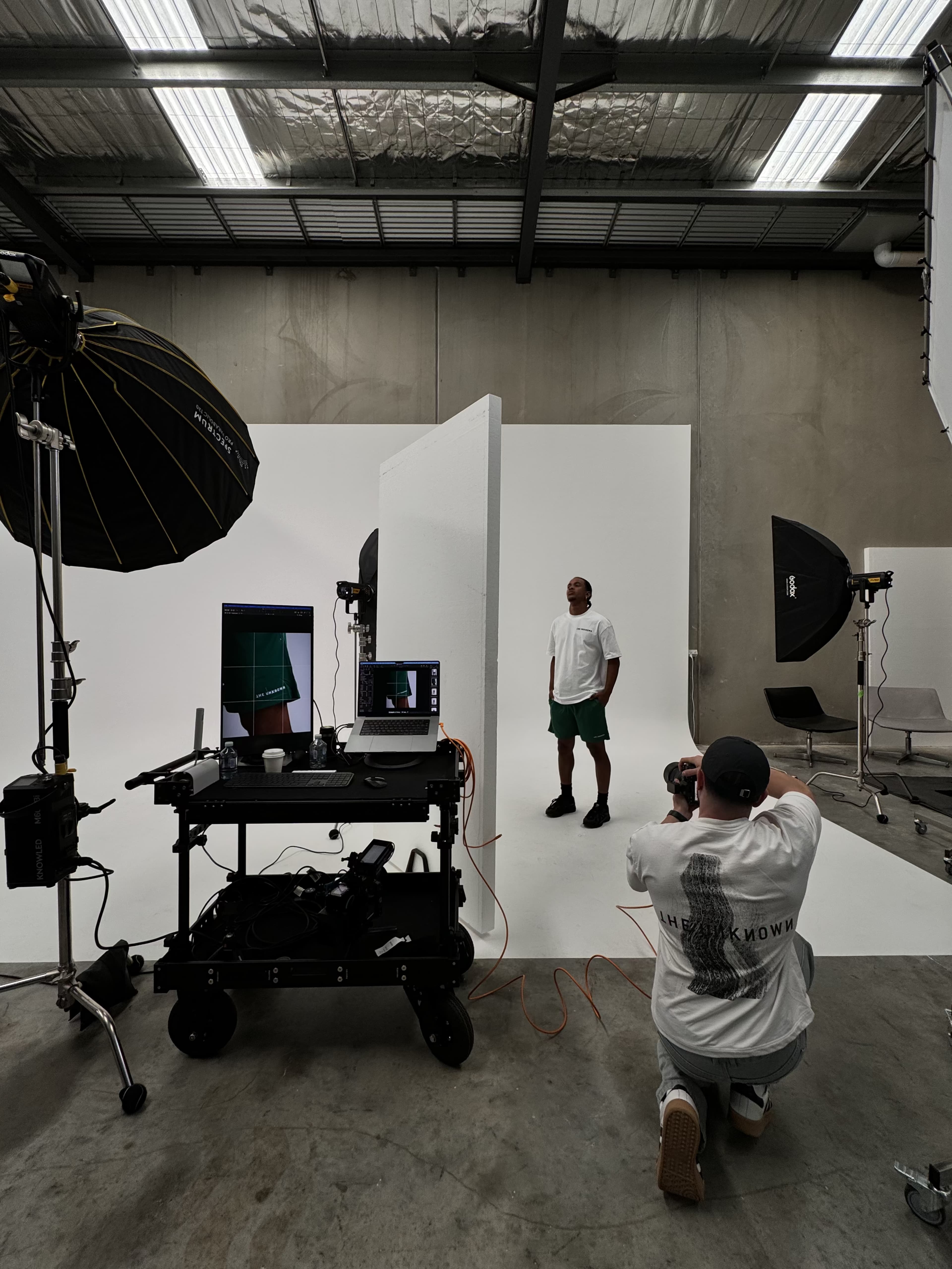 A photographer is capturing a model against a minimalist backdrop in a studio equipped with lighting and camera equipment.