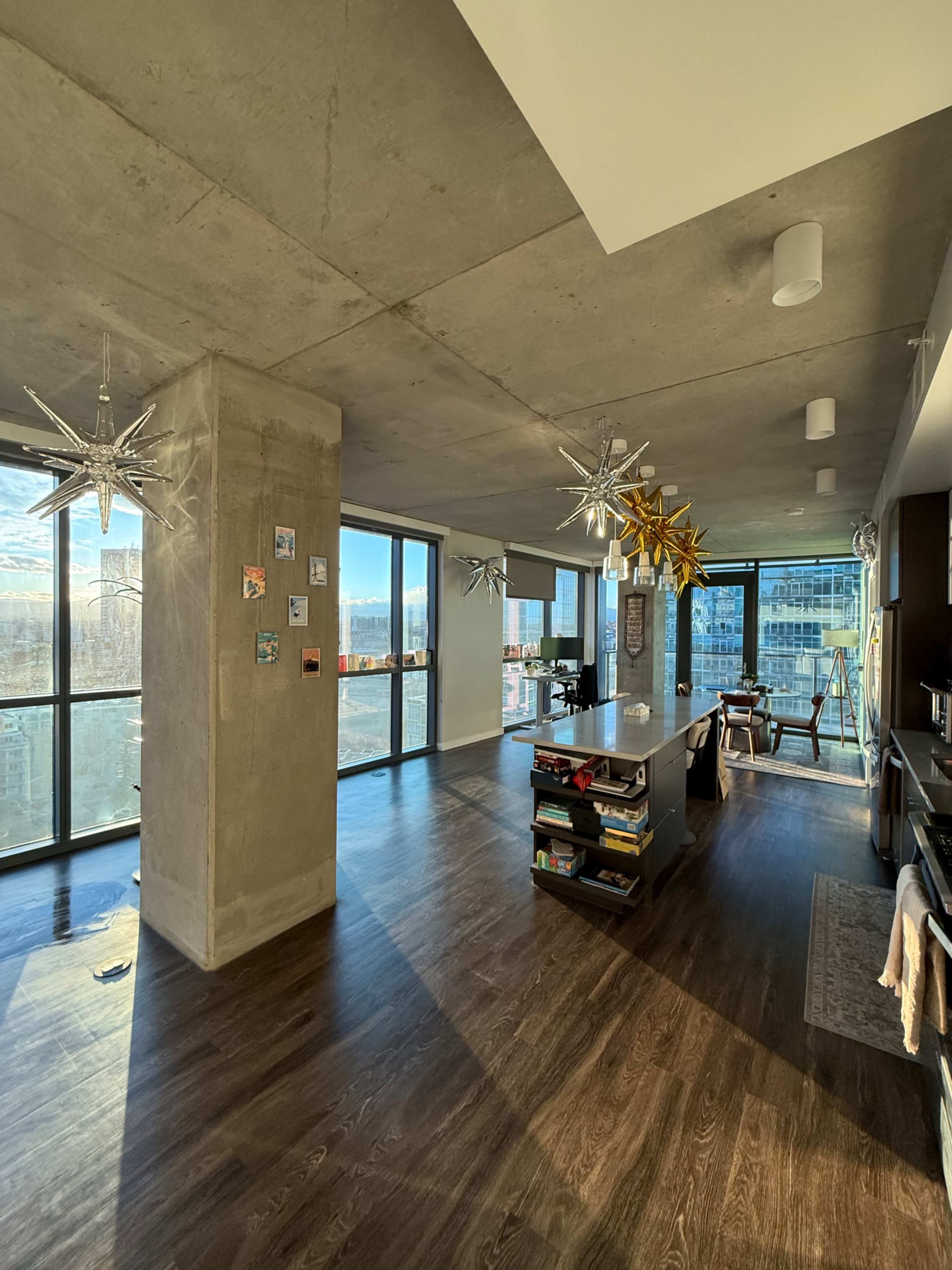 A modern apartment features large windows with a city view, exposed concrete walls, and contemporary lighting fixtures.