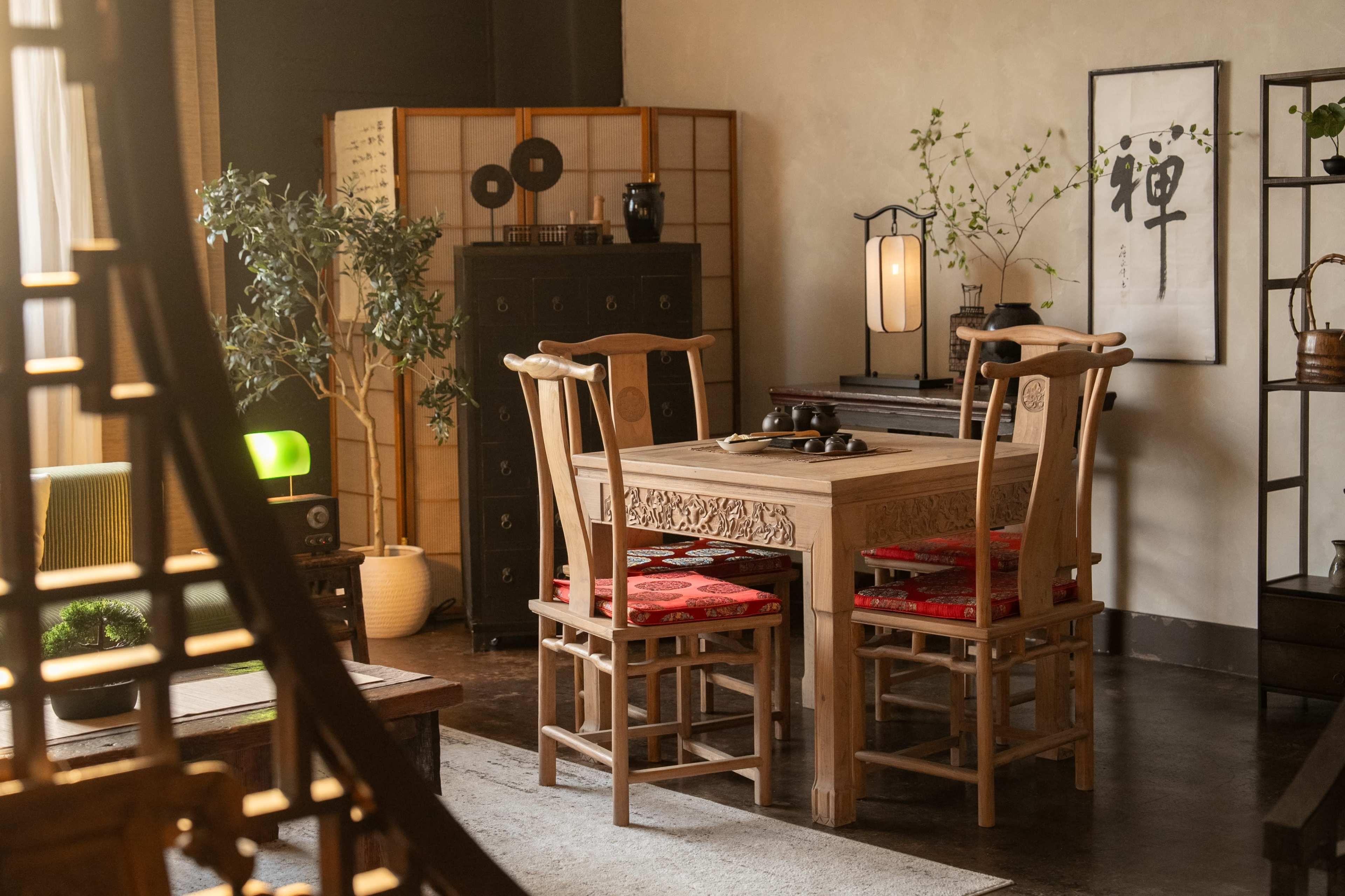 A wooden dining table with red-cushioned chairs is set in a room featuring Asian decor and plants.