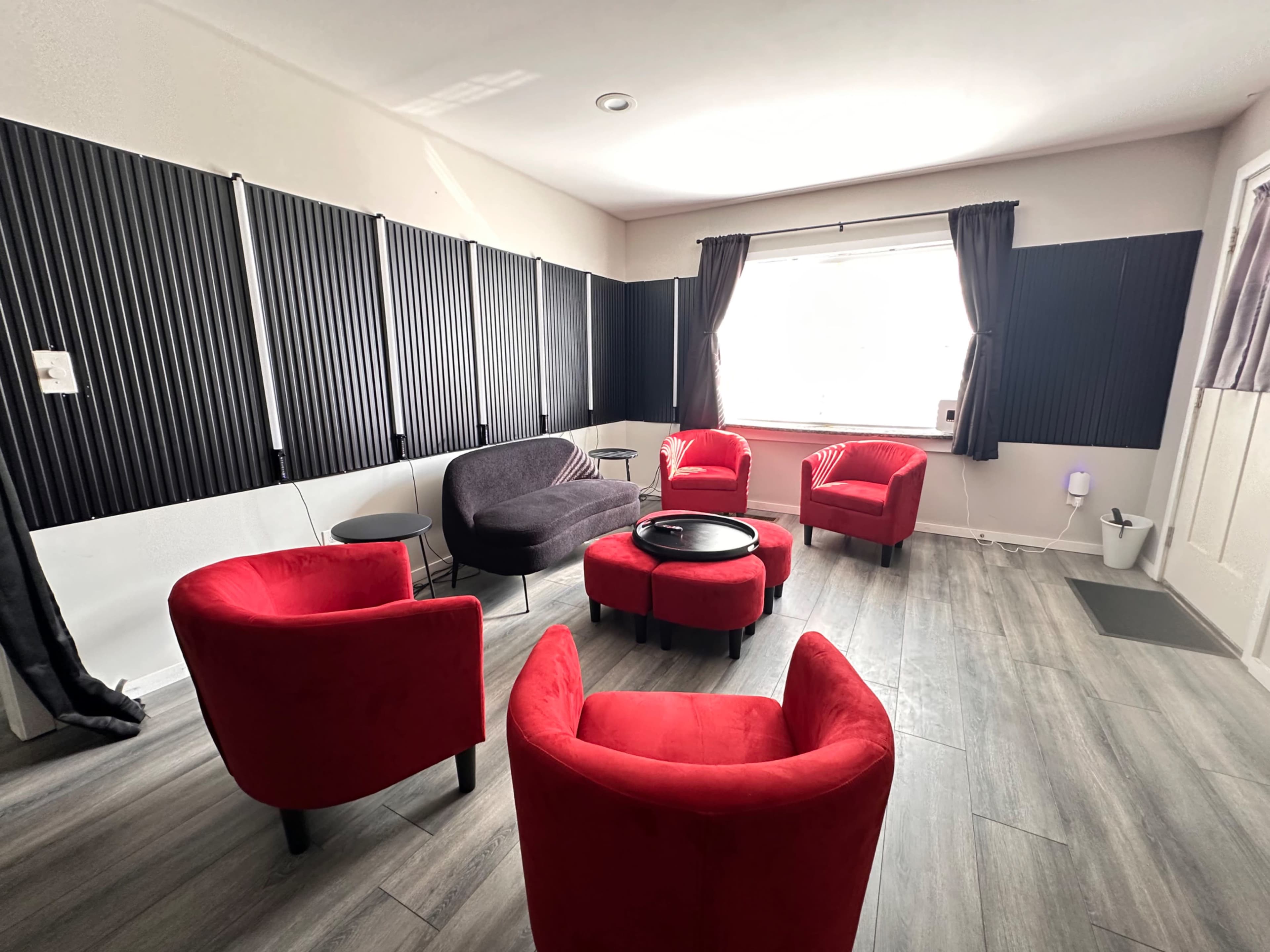The room features four red chairs arranged around a small black table, with a dark sofa against a wall and soundproof panels lining the walls.