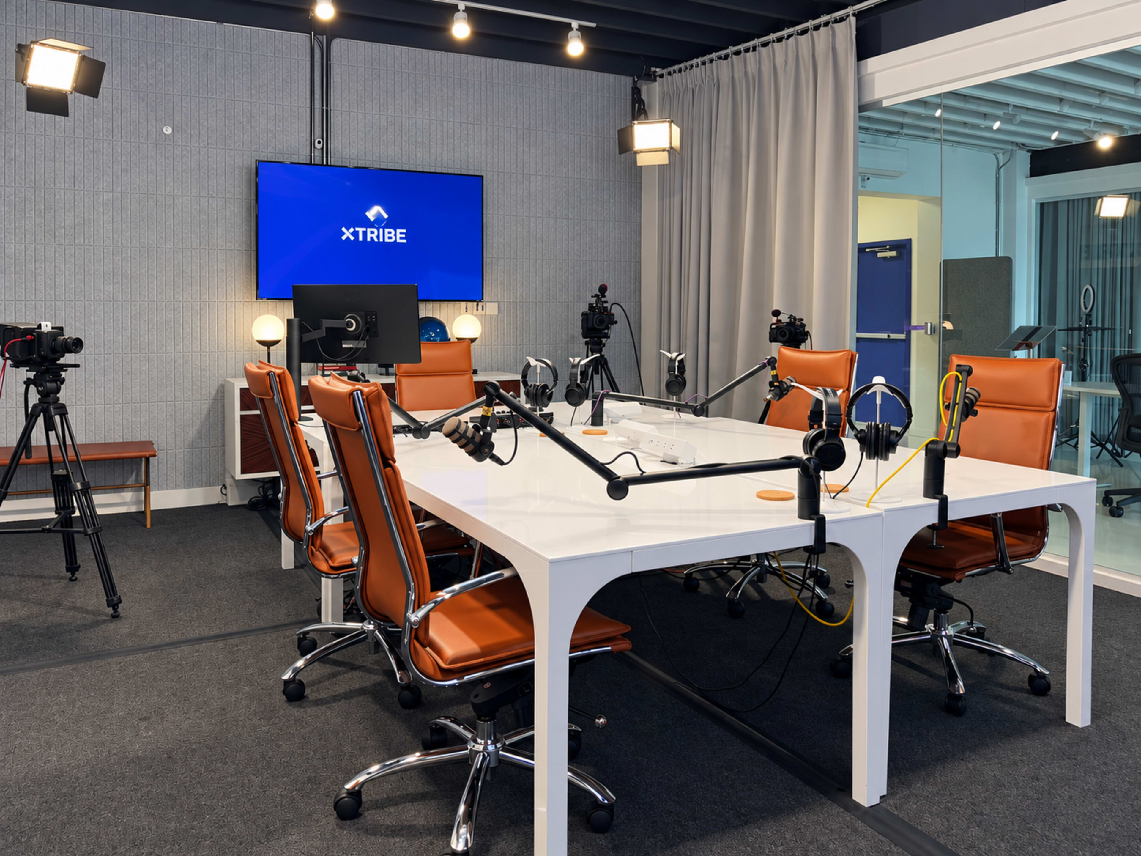The image shows a modern podcast recording studio with a large white table, several microphones, and multiple cameras set up for recording.