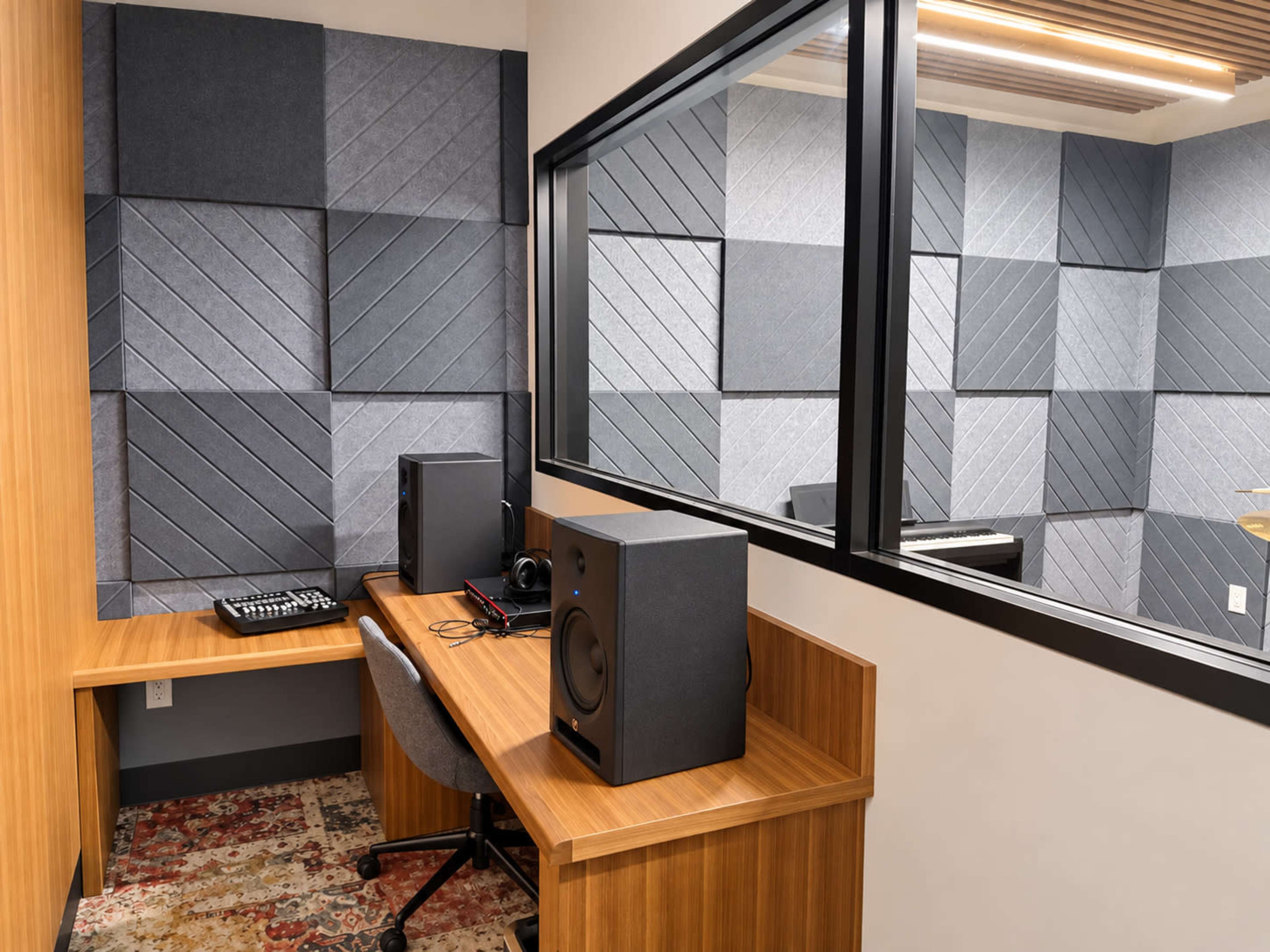 The image shows a soundproof recording studio featuring a wooden desk with audio equipment, including speakers and a mixer, along with sound-absorbing wall panels.