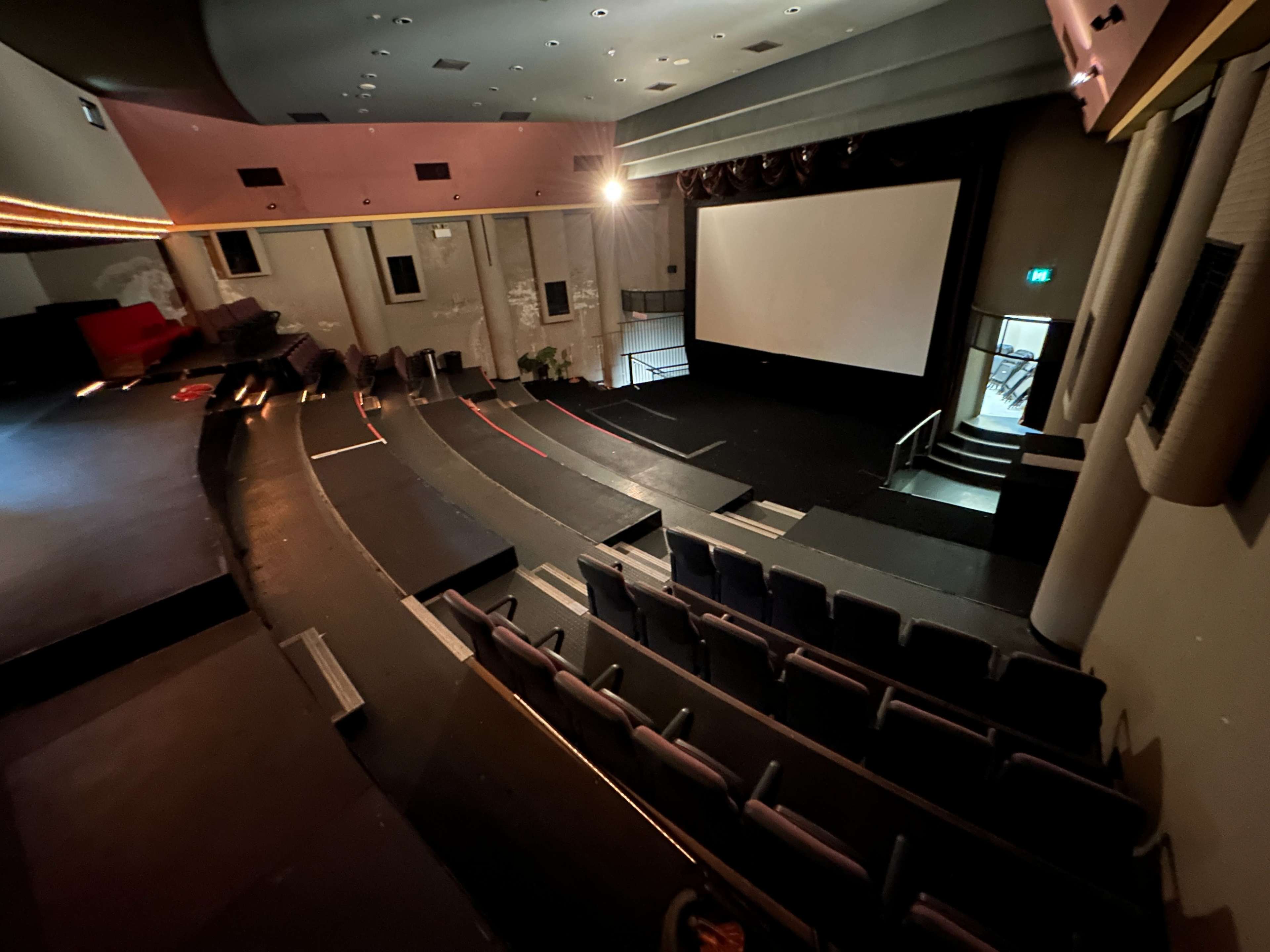 An empty auditorium with tiered seating facing a large screen, illuminated by soft lighting.