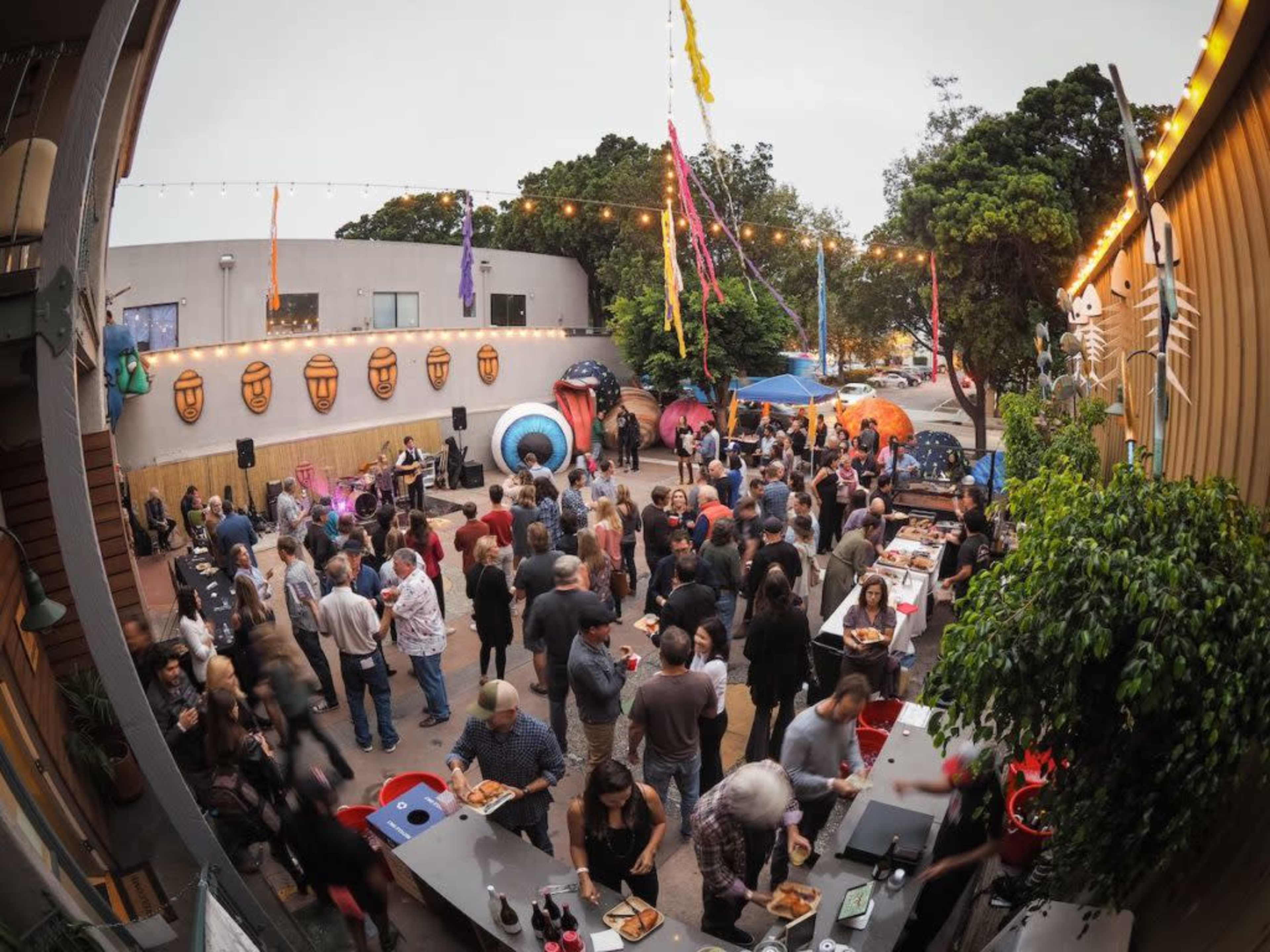 A crowd of people gathers at an outdoor event featuring music, food stalls, and colorful decorations.