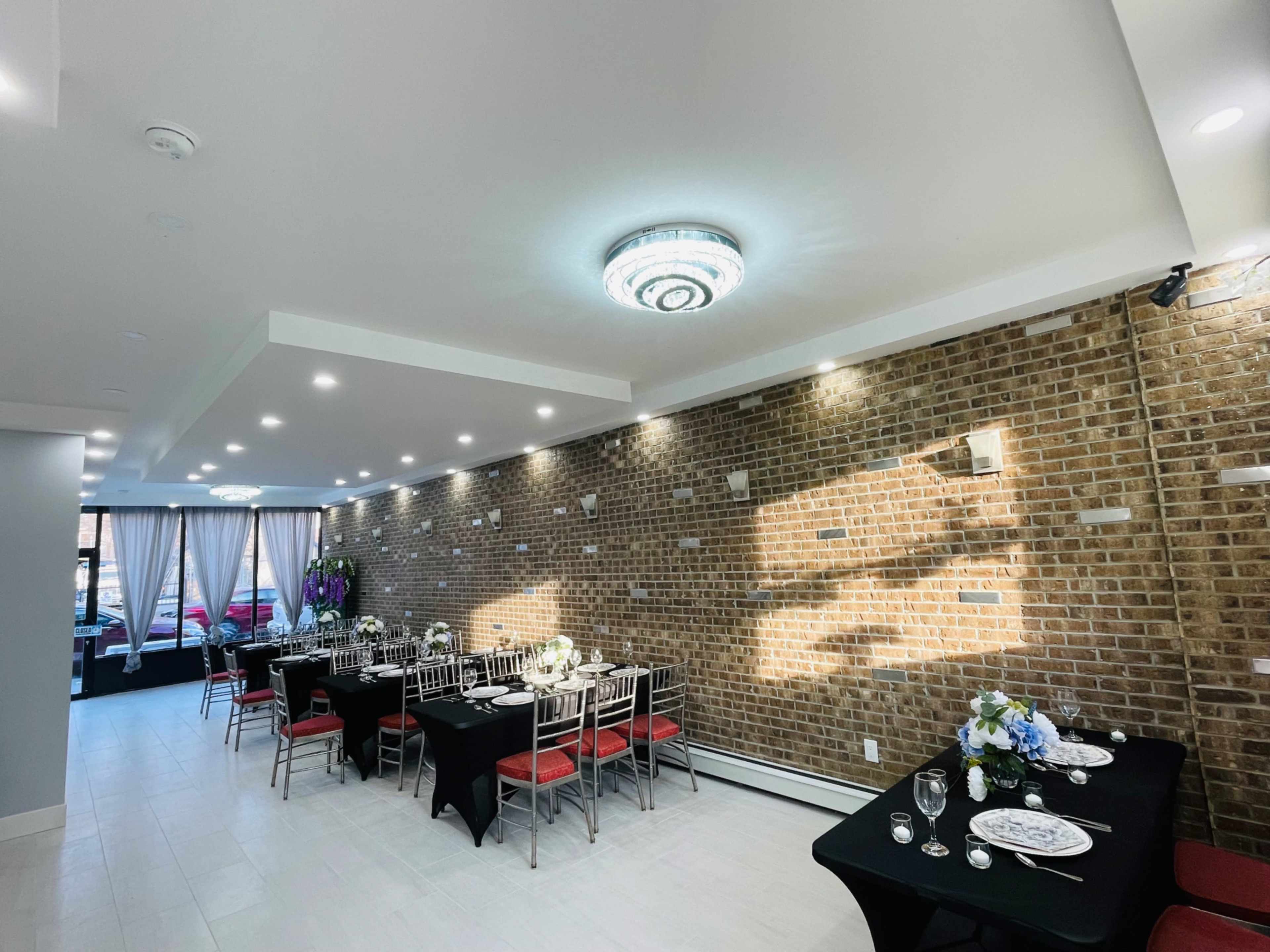 A dining area with two long tables set for a meal, surrounded by brick walls and lit by modern ceiling lights.
