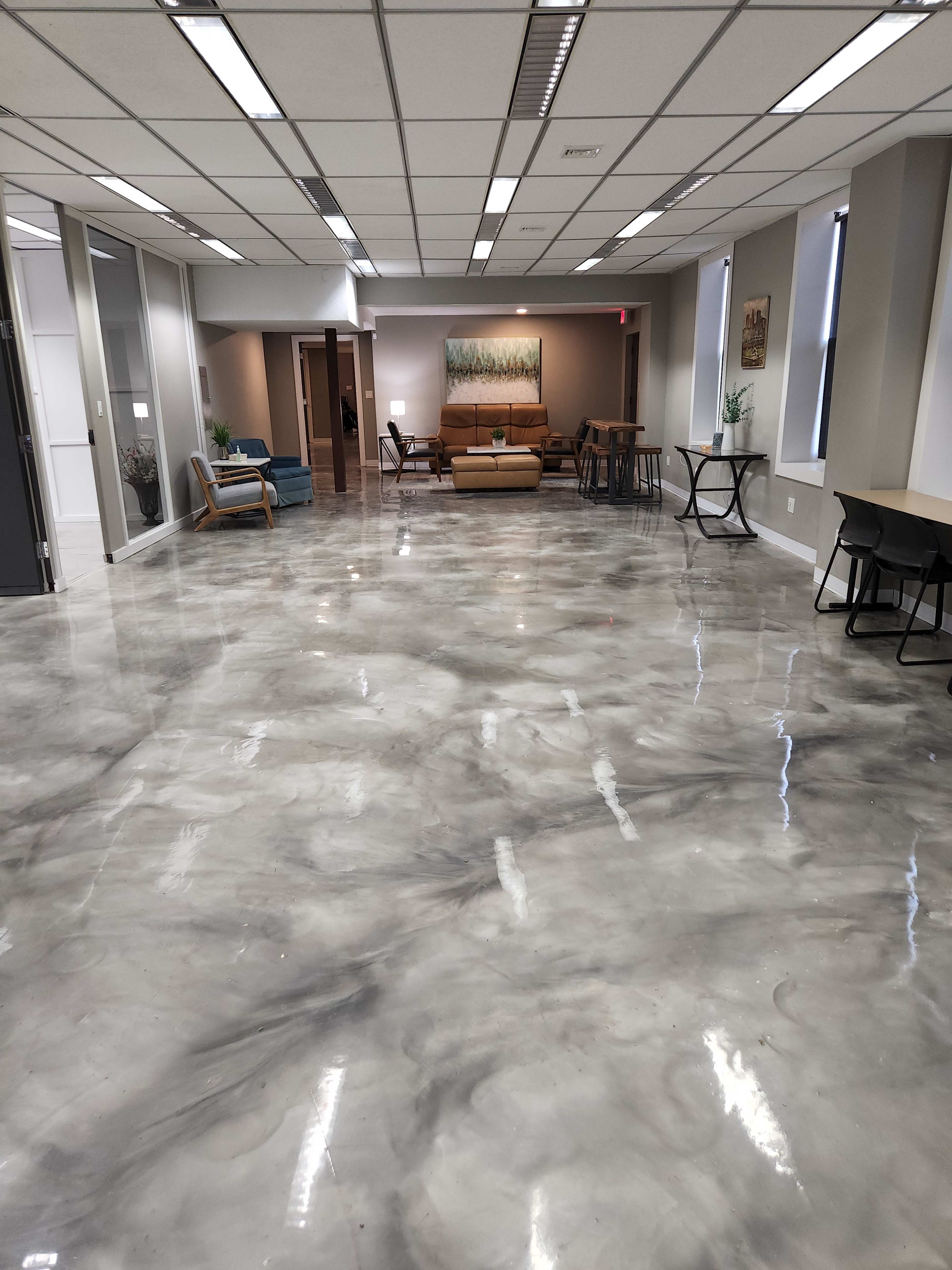 The image shows a spacious, modern office area with polished gray marble flooring and a few seating arrangements.