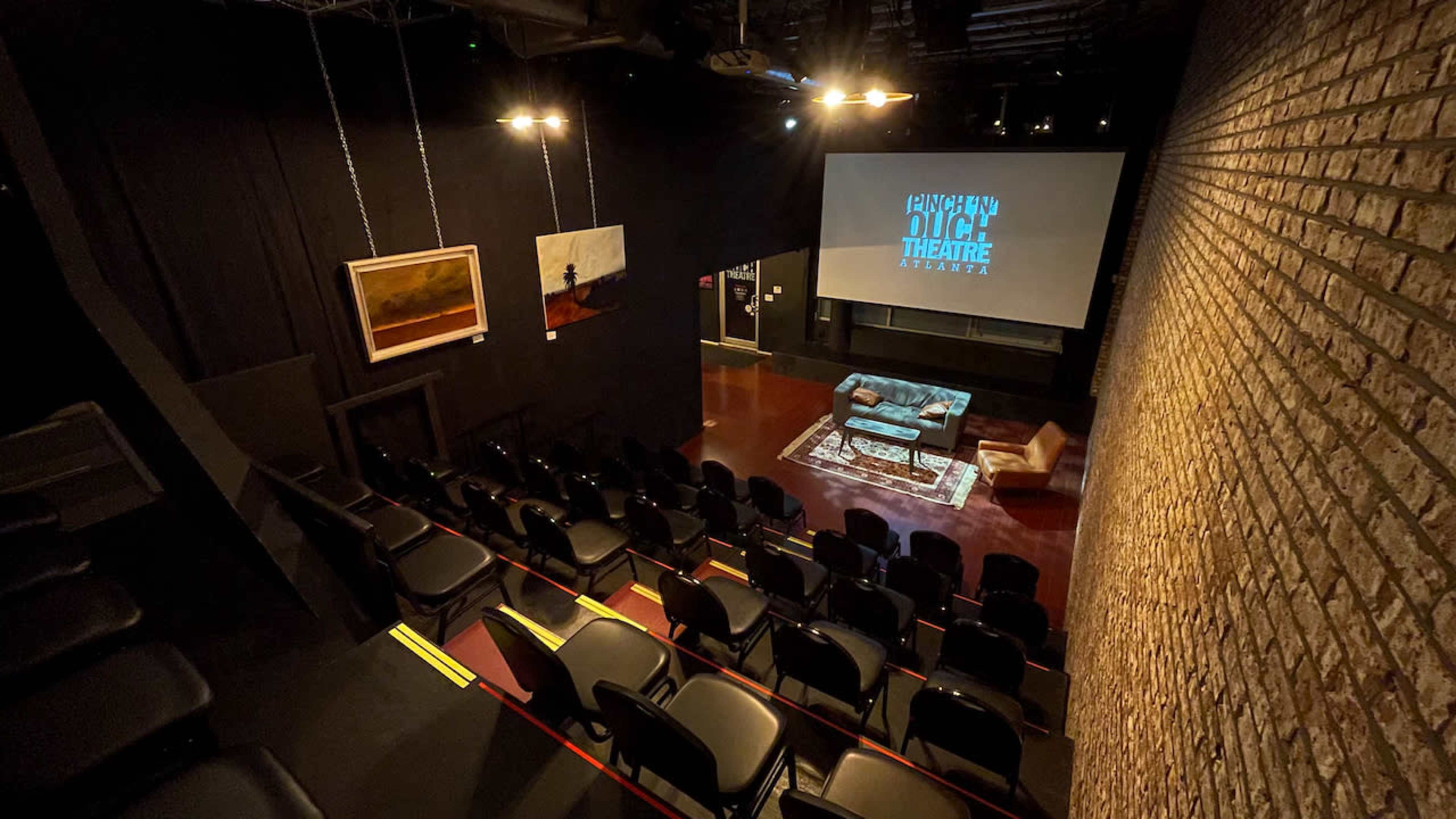 The image shows an empty theater with black seating, exposed brick walls, and a large screen displaying "DUTCH THEATRE" at the front.