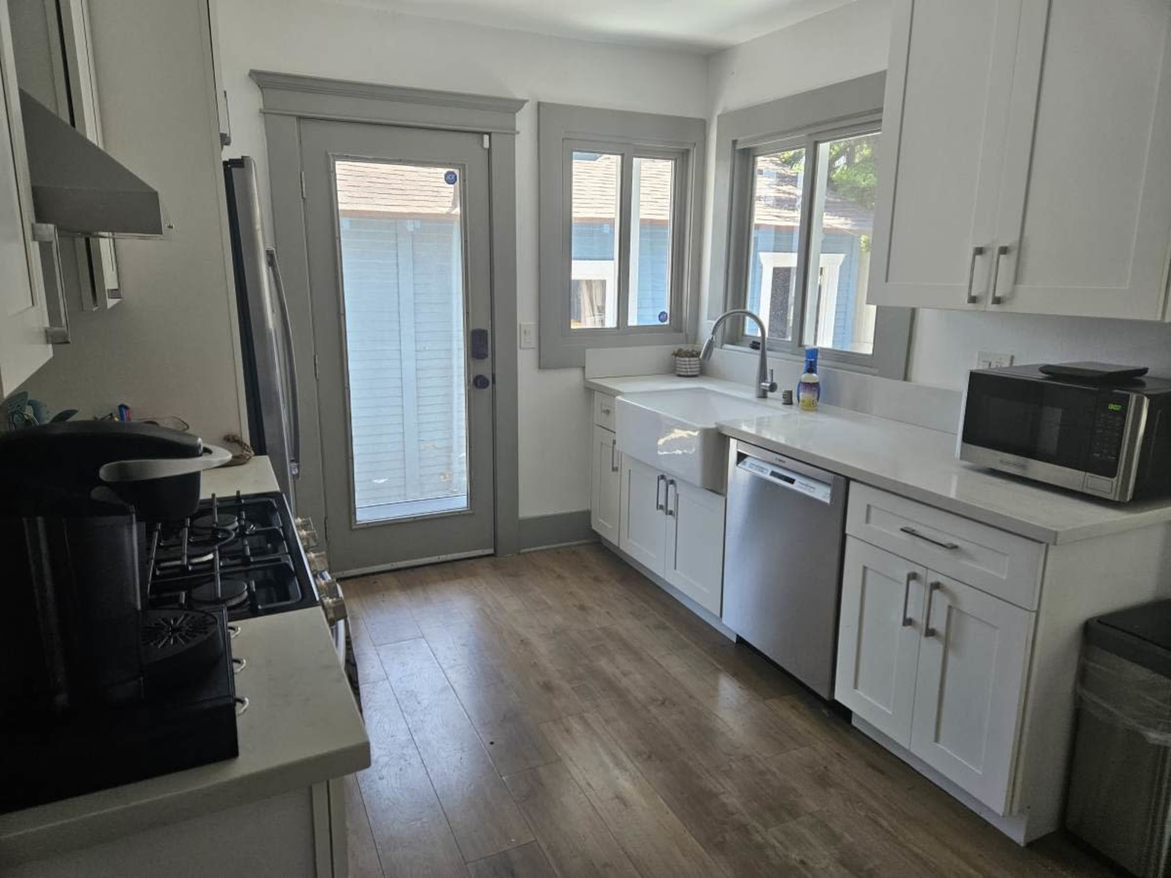 The image shows a modern kitchen with white cabinetry, stainless steel appliances, and a door leading outside.