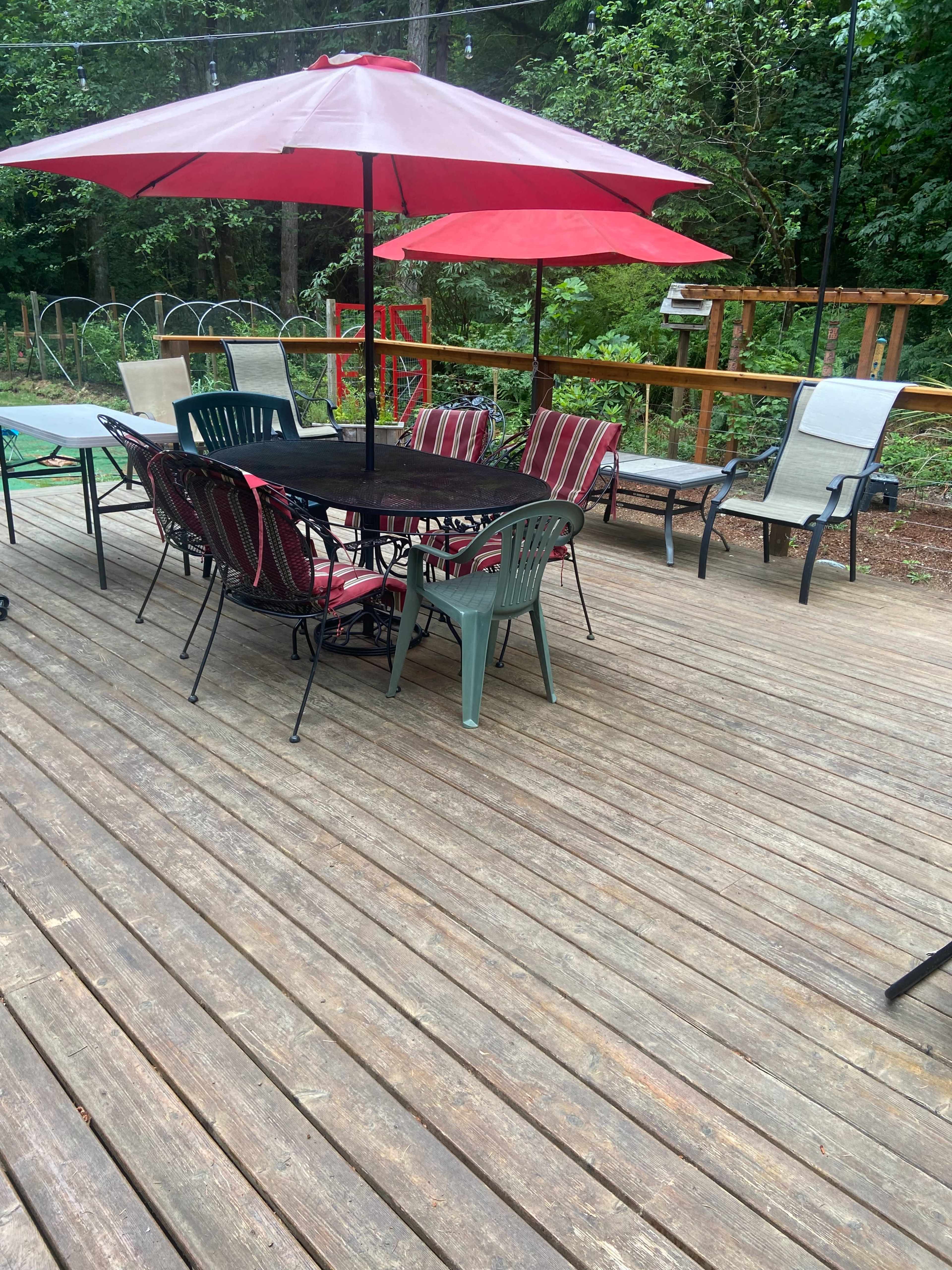 A deck area is set up with various chairs and tables under a red umbrella, surrounded by greenery.