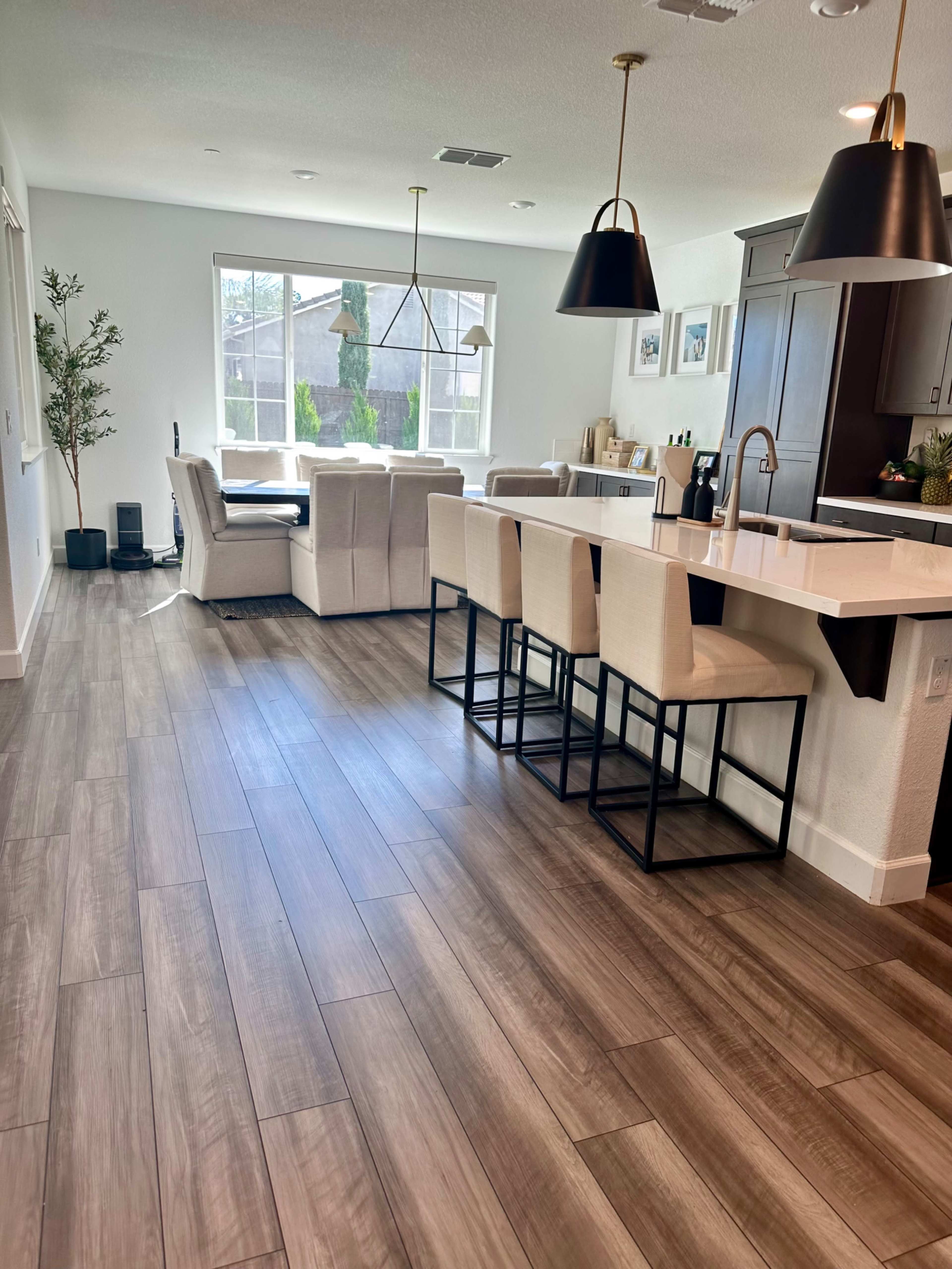 The image shows a modern open-concept kitchen and living area with a large window, bar stools at the kitchen island, and a seating arrangement in the living space.