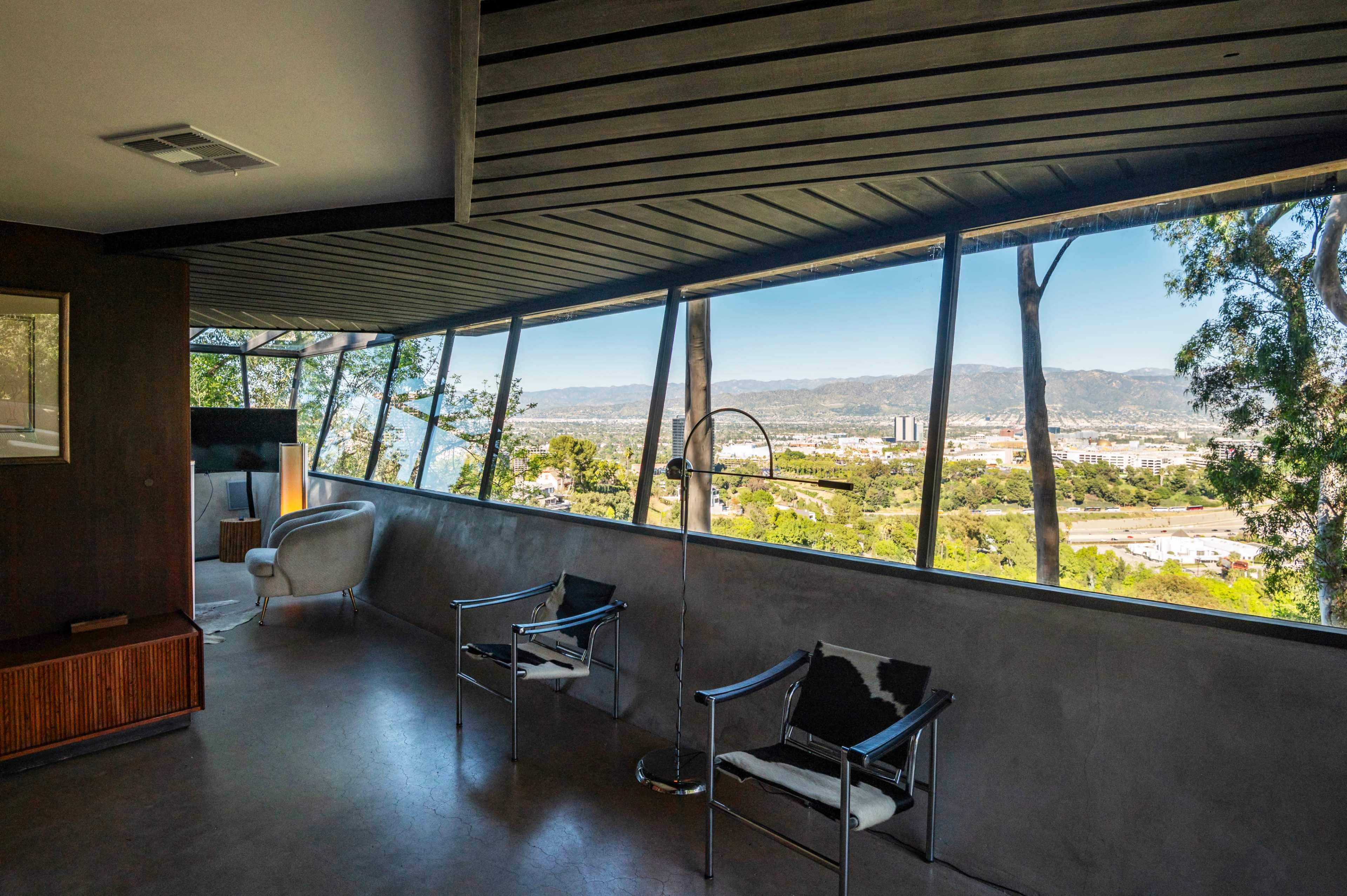 The image shows a modern interior space with large windows offering a panoramic view of a mountainous landscape and city below.