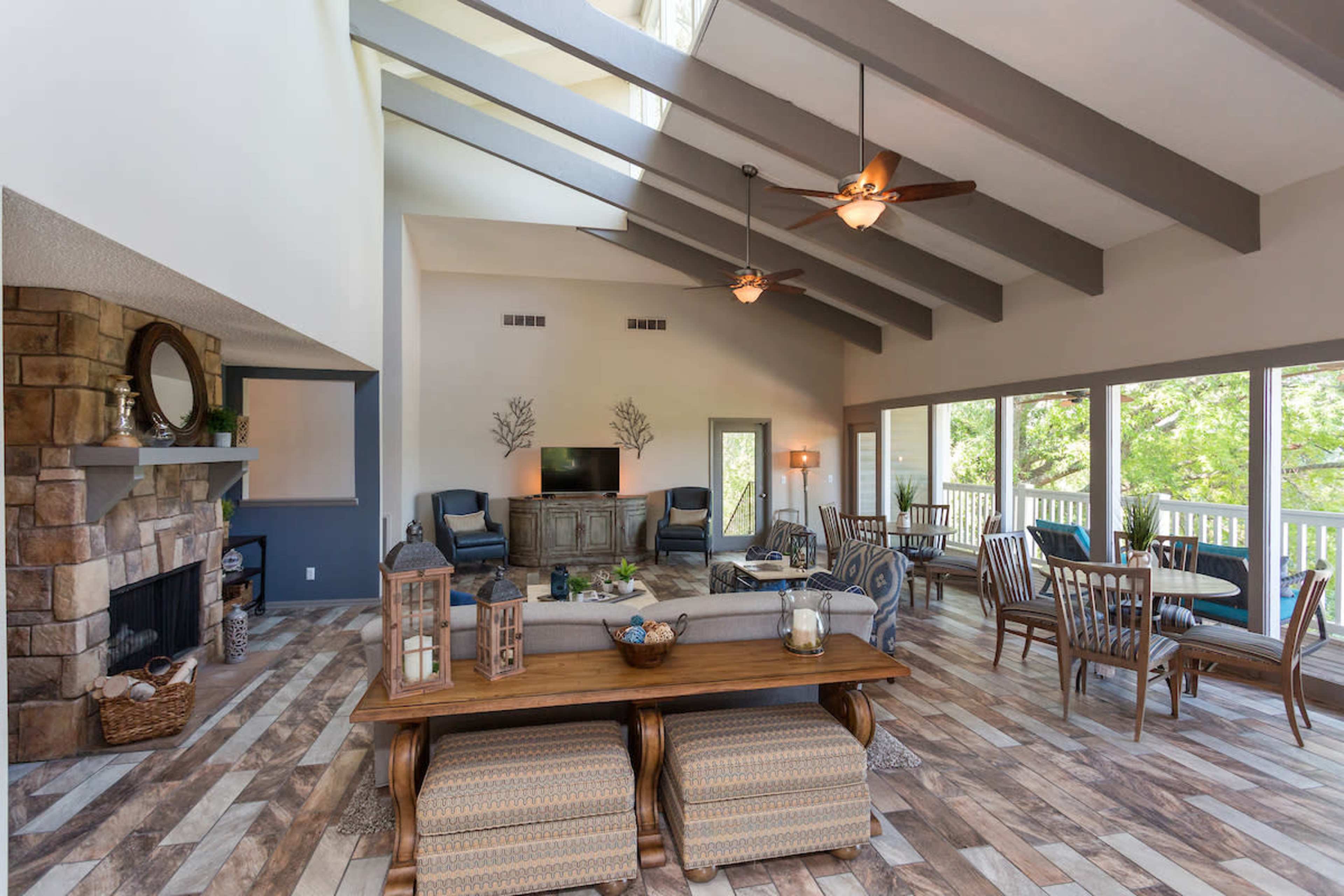 A spacious living area with vaulted ceilings, large windows, a stone fireplace, and a dining table surrounded by chairs.