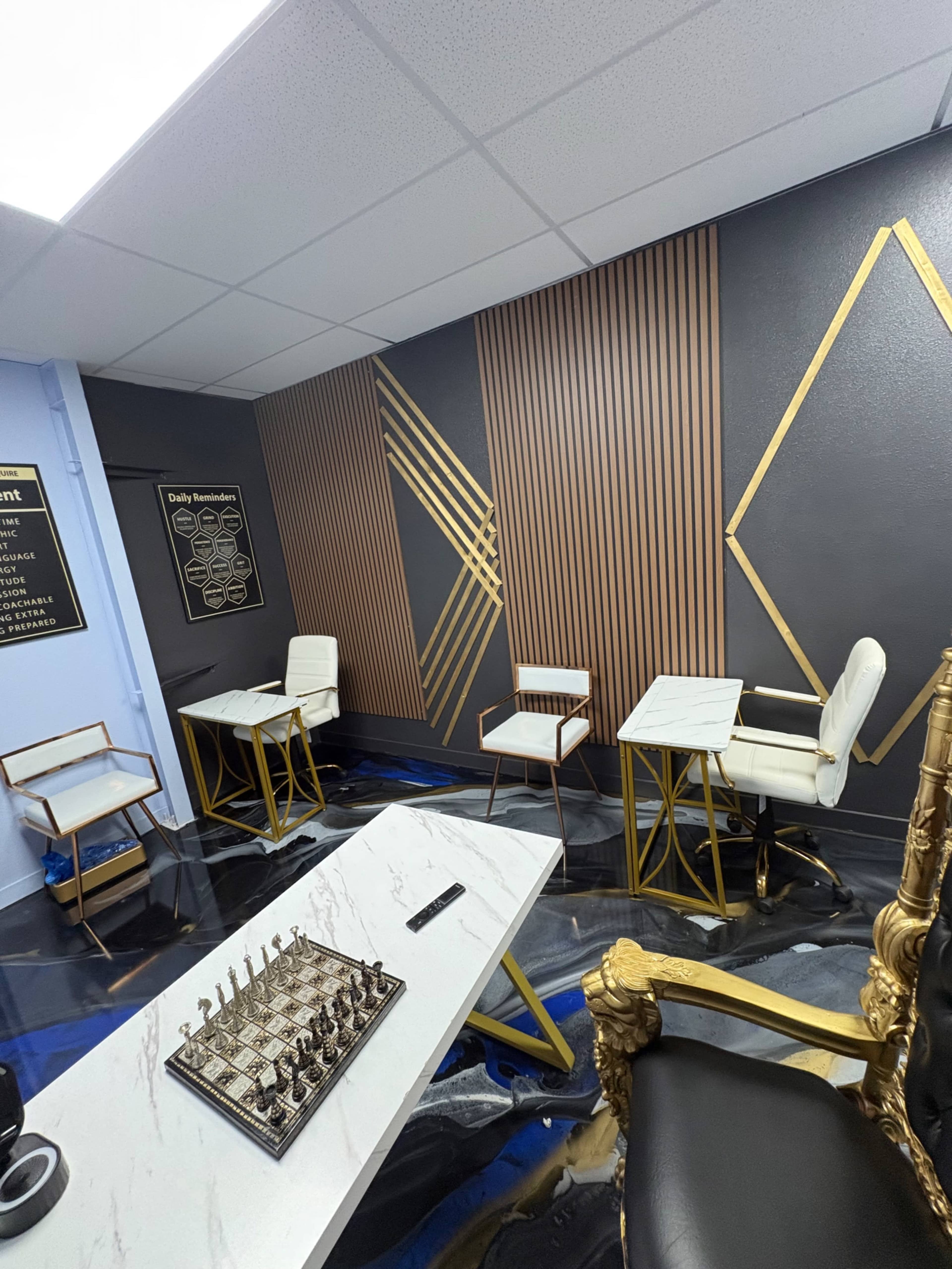 The image shows a modern interior with a chessboard on a white table, gold and black accents on the walls, and stylish seating areas.