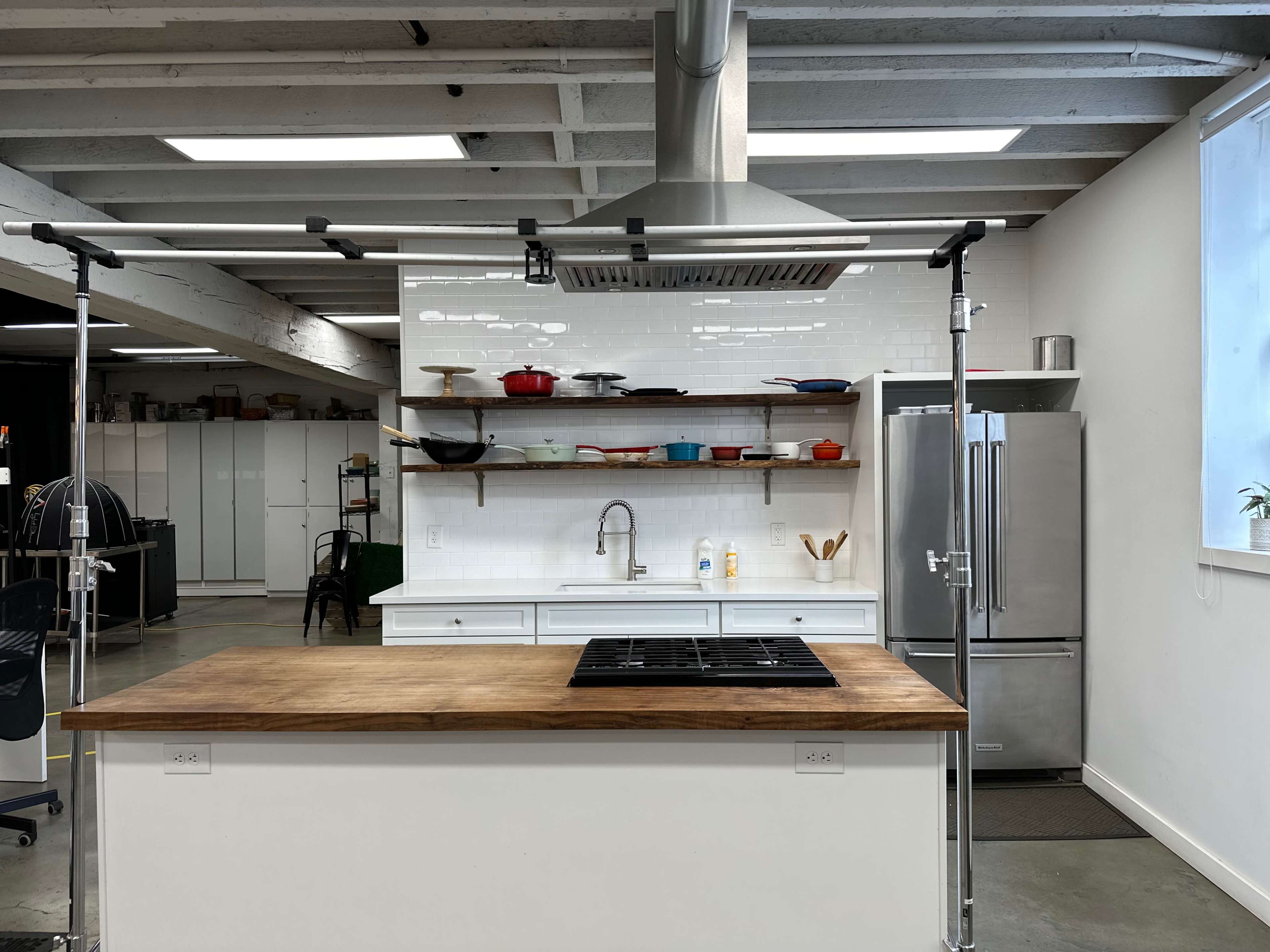 A modern kitchen features a central island with a gas cooktop, stainless steel appliances, and open shelving displaying cookware.