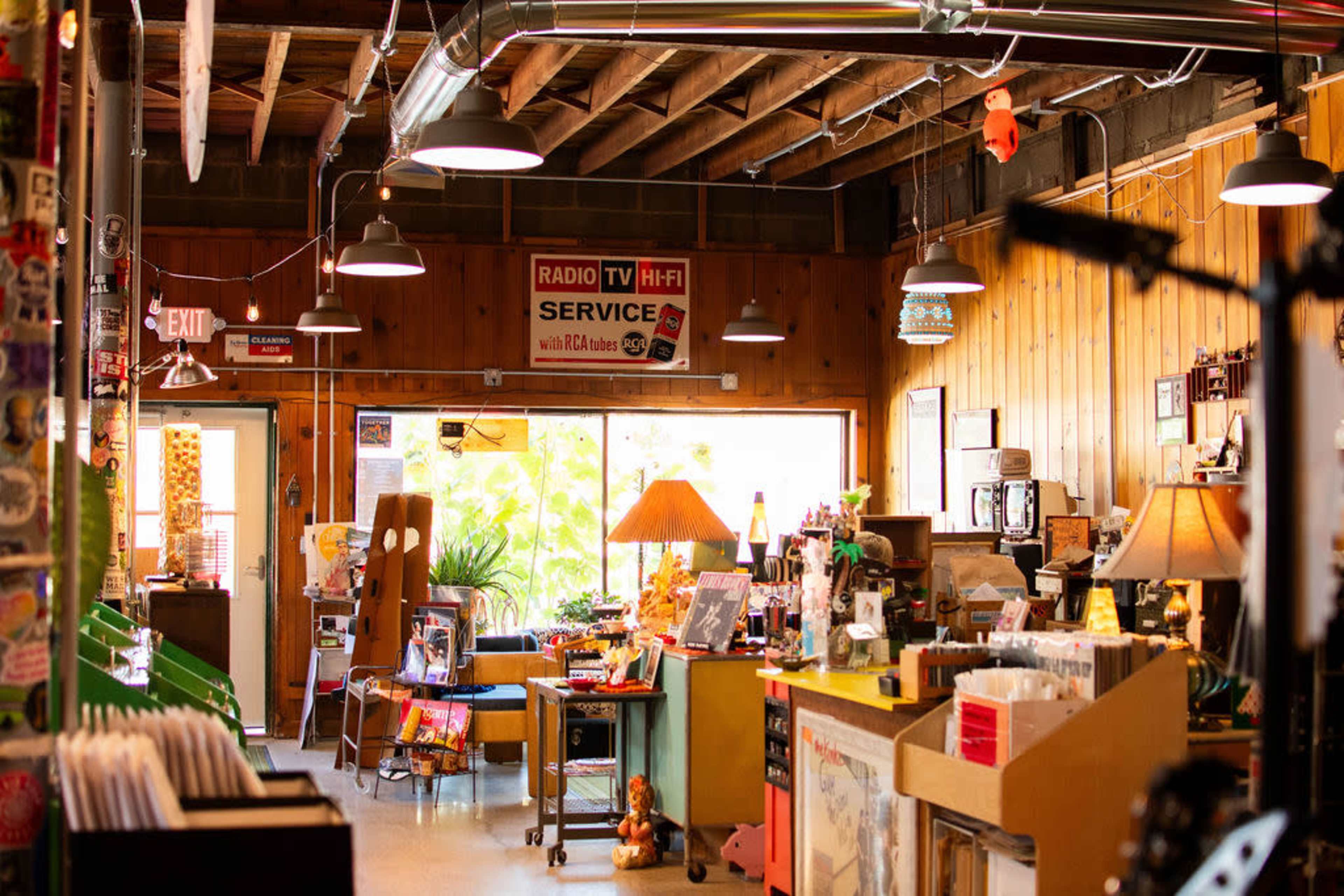 The image shows an eclectic vintage shop with wooden paneling, various items for sale, and bright lighting from several hanging lamps.