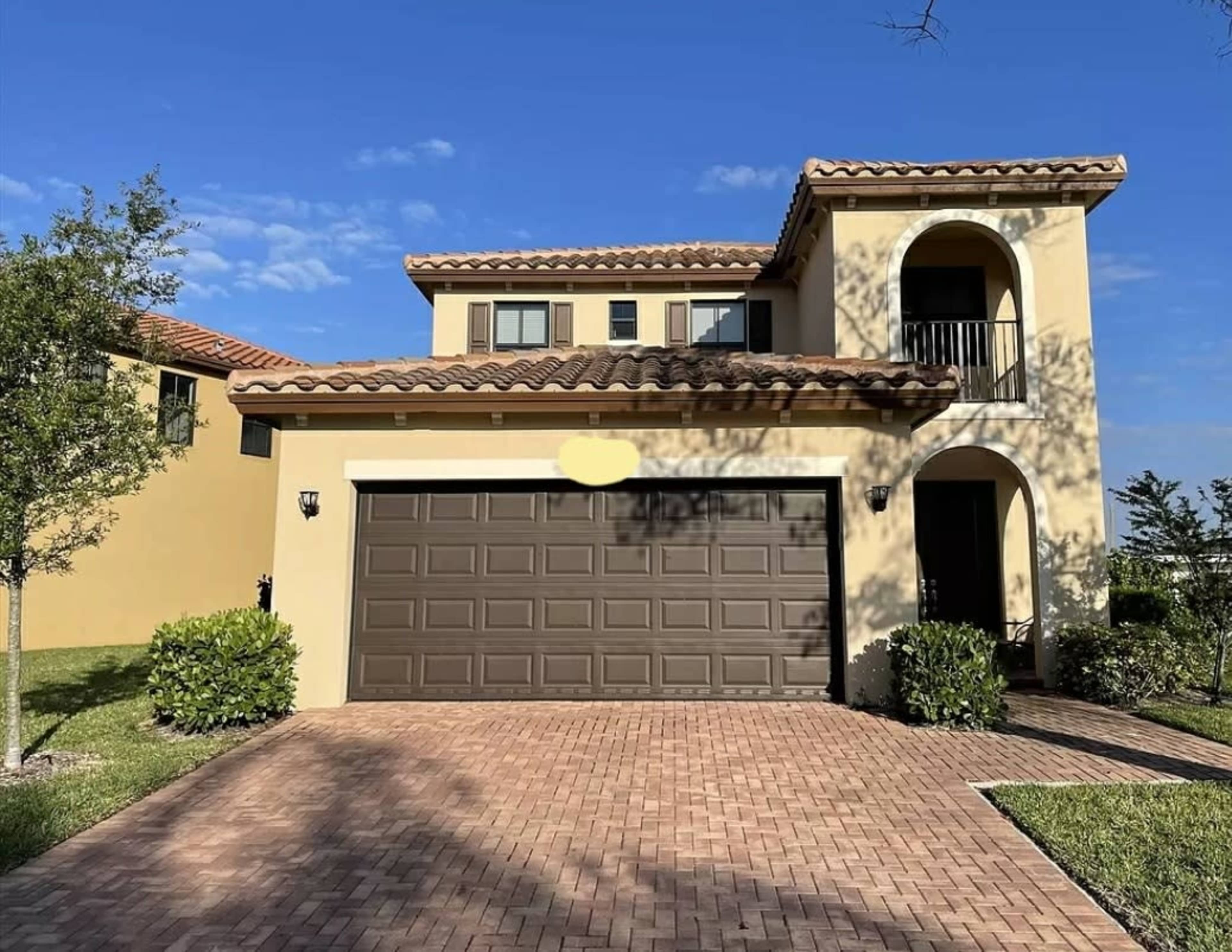 A two-story house with a brown garage door and a brick driveway is set against a blue sky.