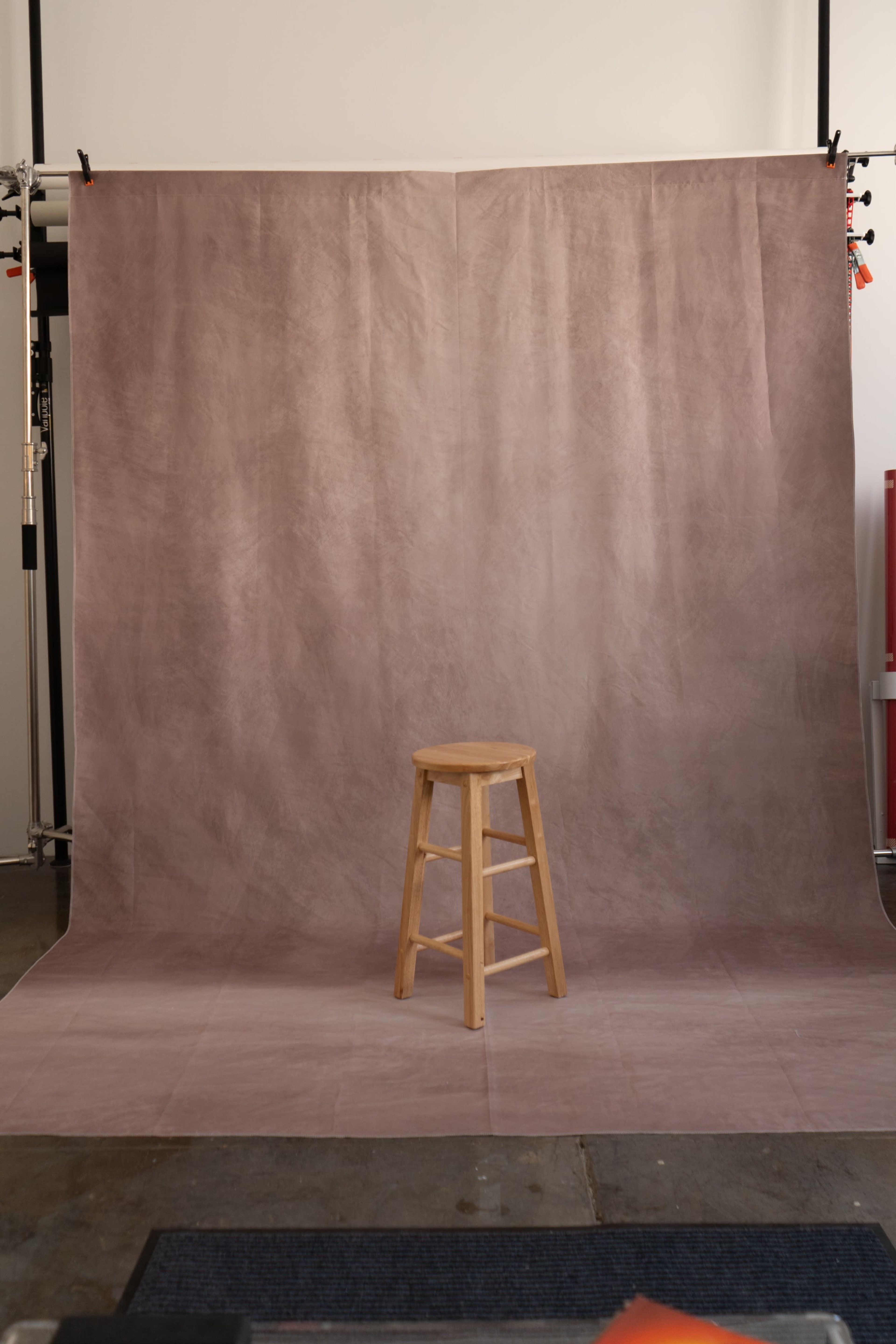 The image shows a wooden stool placed in front of a soft, muted backdrop in a photography studio.