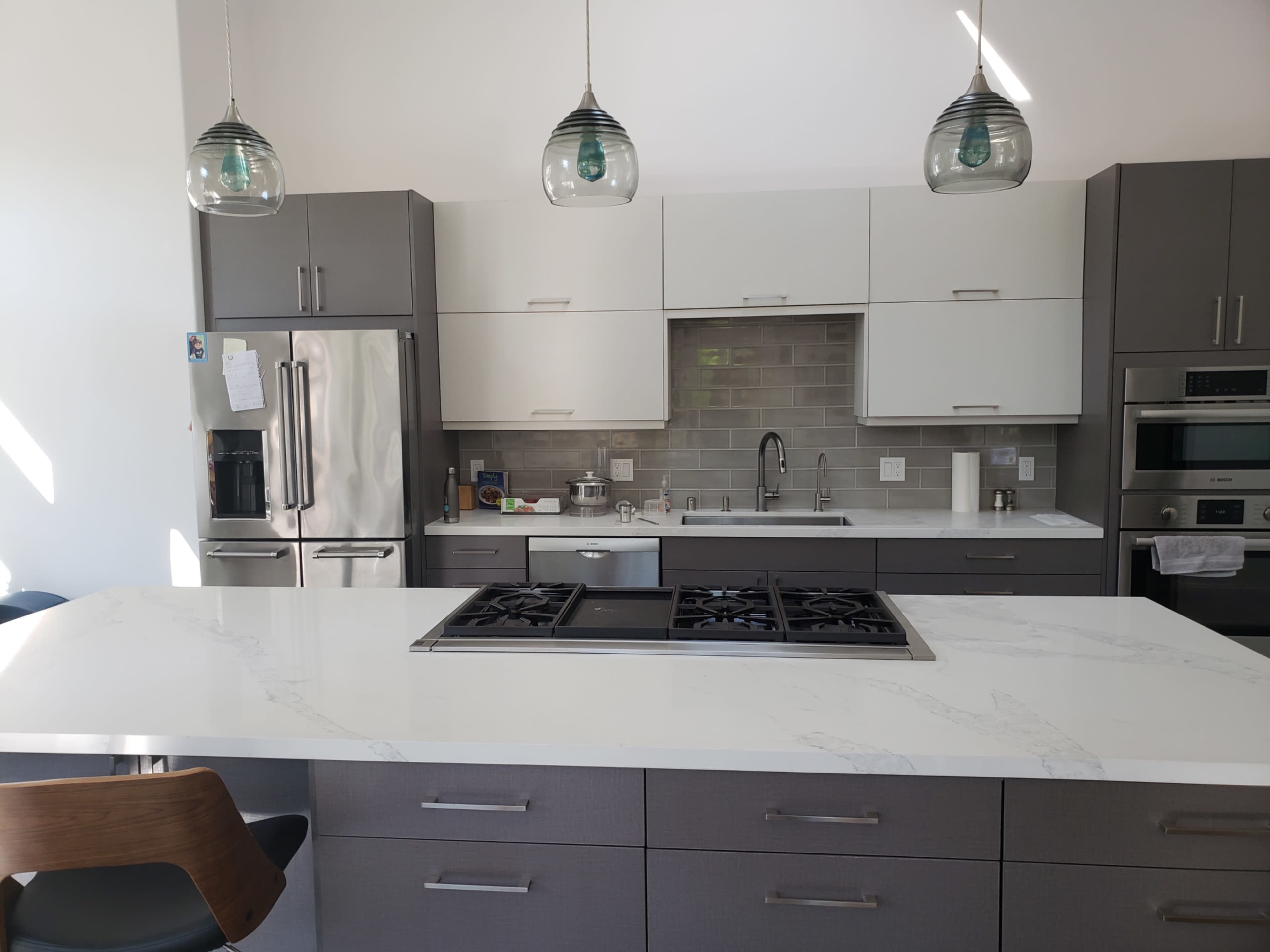 A modern kitchen with gray and white cabinetry, a central island featuring a gas cooktop, and pendant lights hanging above.