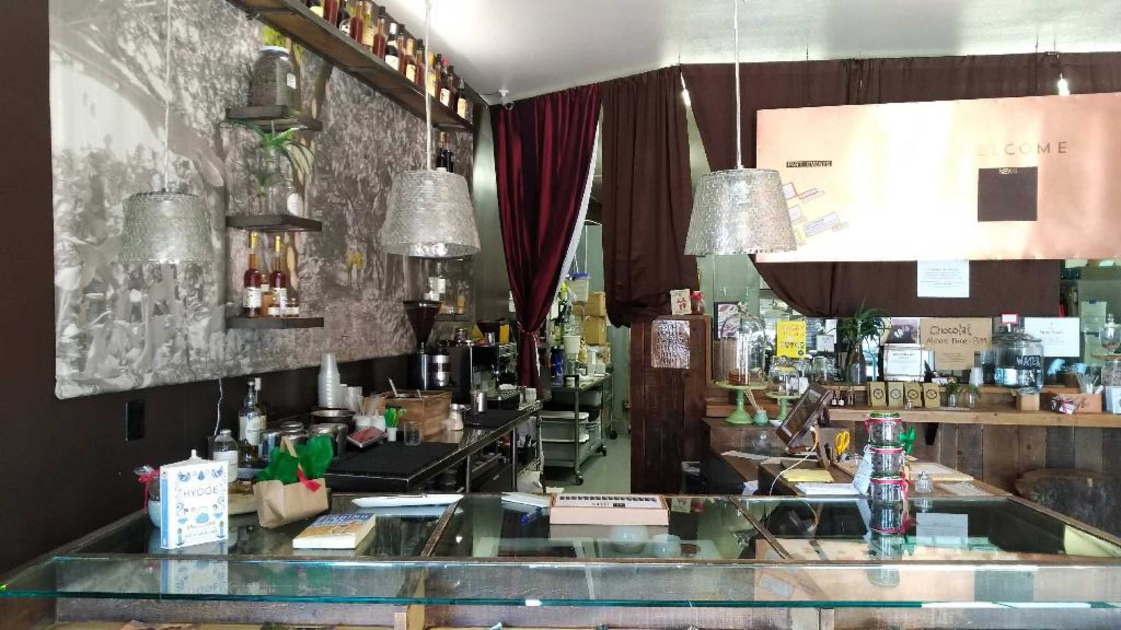 A coffee shop interior with a counter displaying various beverages, shelves lined with bottles, and dim lighting from pendant lamps.