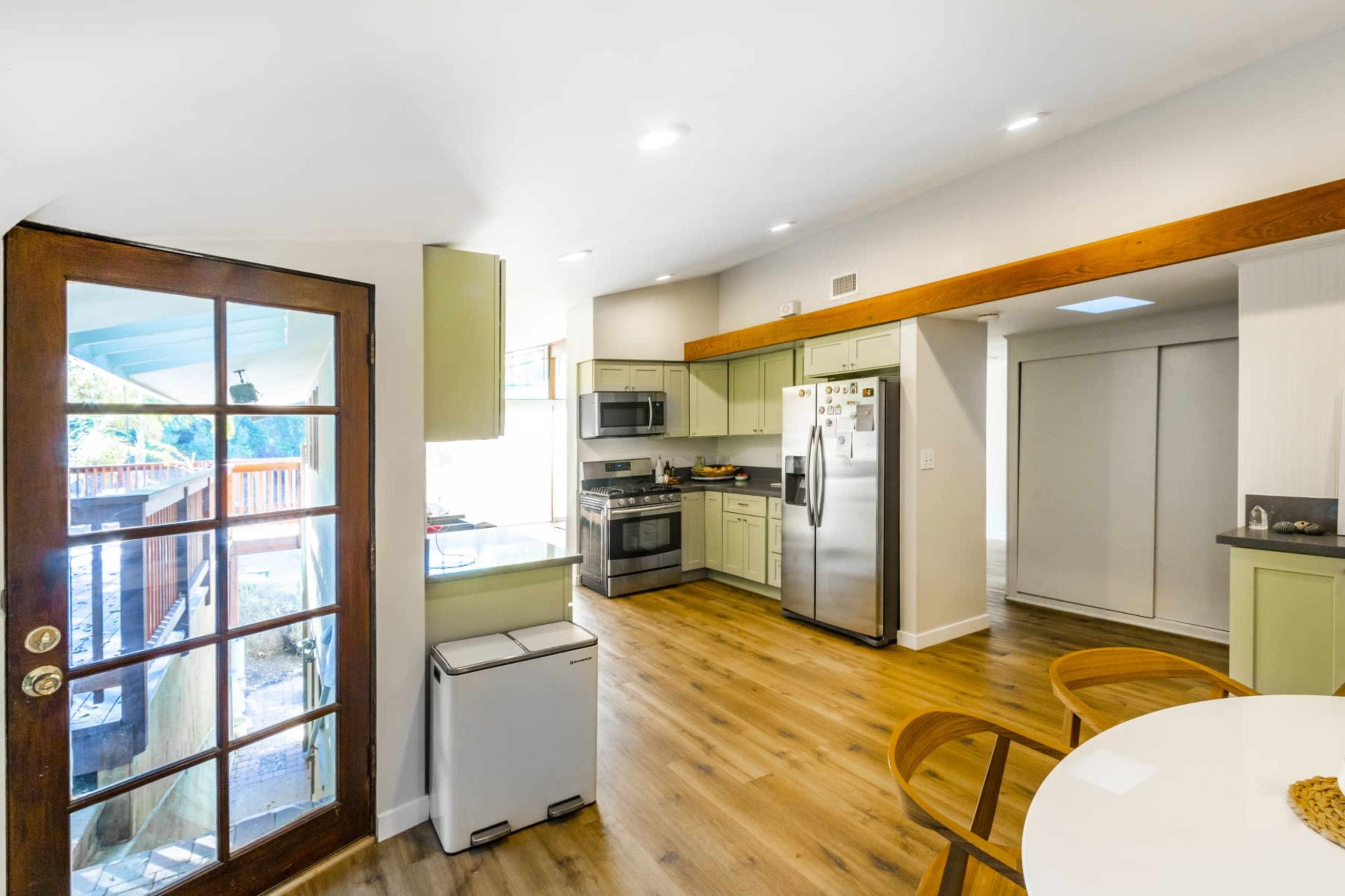 The kitchen features modern appliances, wooden flooring, and an open layout with a sliding glass door leading outside.