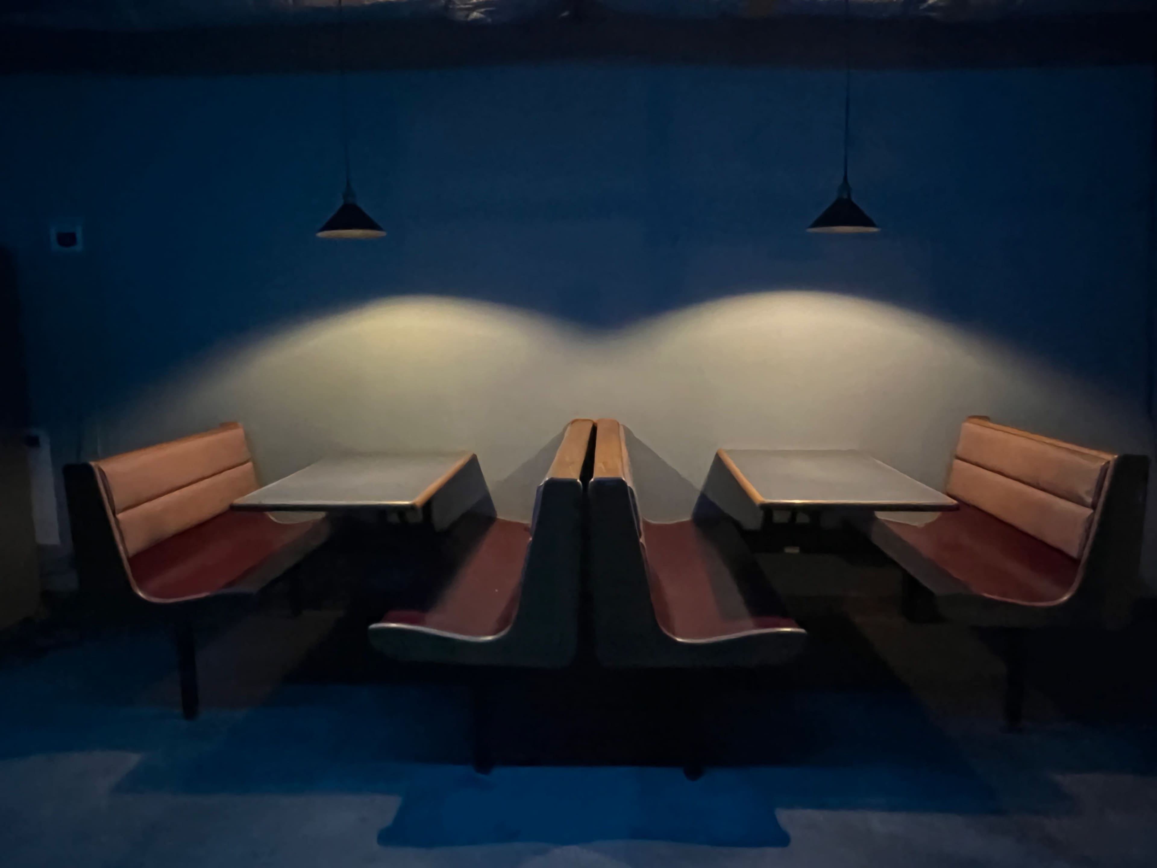 The image features a dimly lit room with two booth seating areas facing each other, each with a table in the center.