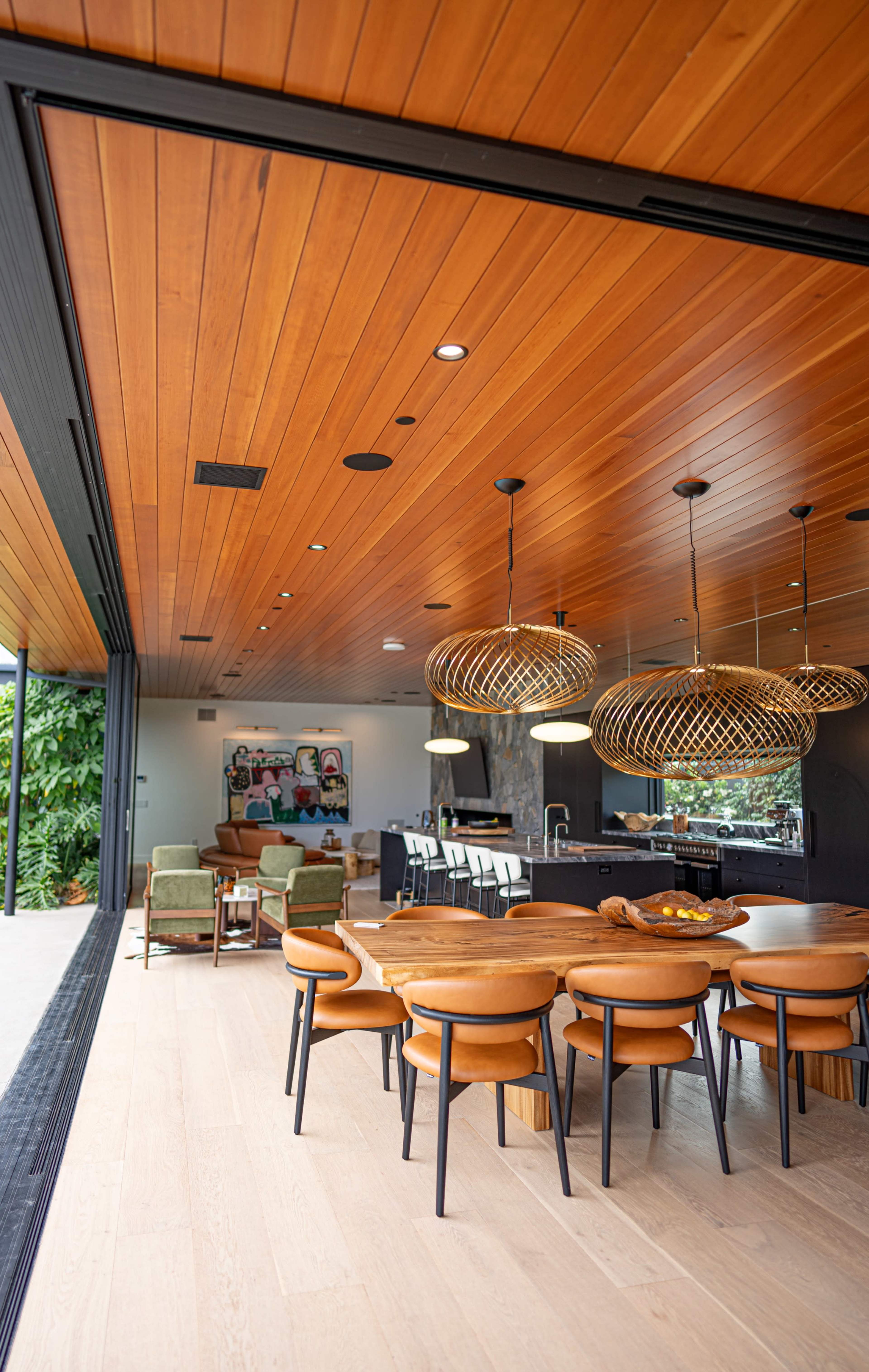 A modern interior space featuring a dining area with a circular wooden table and chairs, large pendant lights, and an open view connecting to a living area.