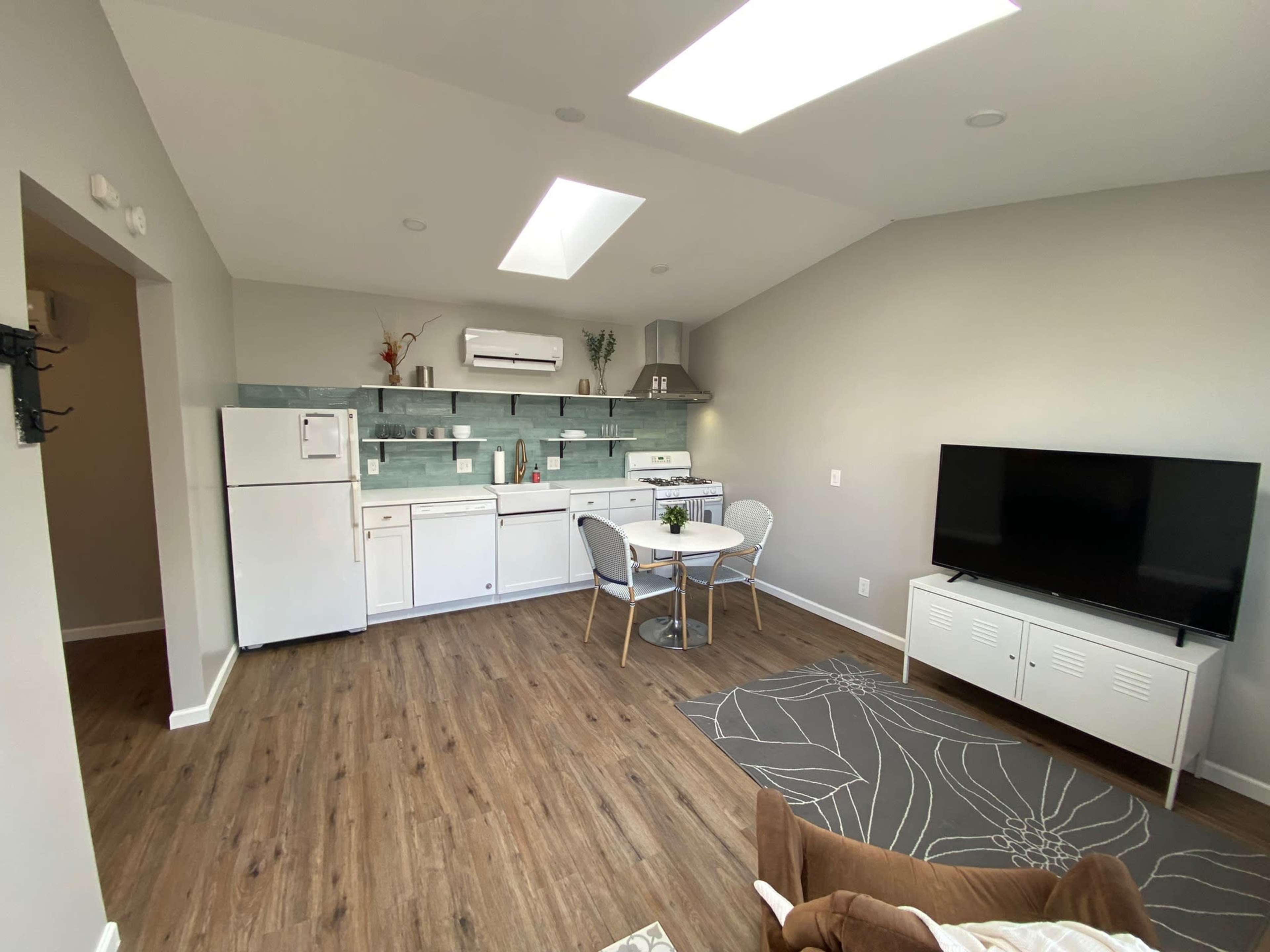 A modern kitchen and living area is shown, featuring a dining table with chairs, a refrigerator, and a television.