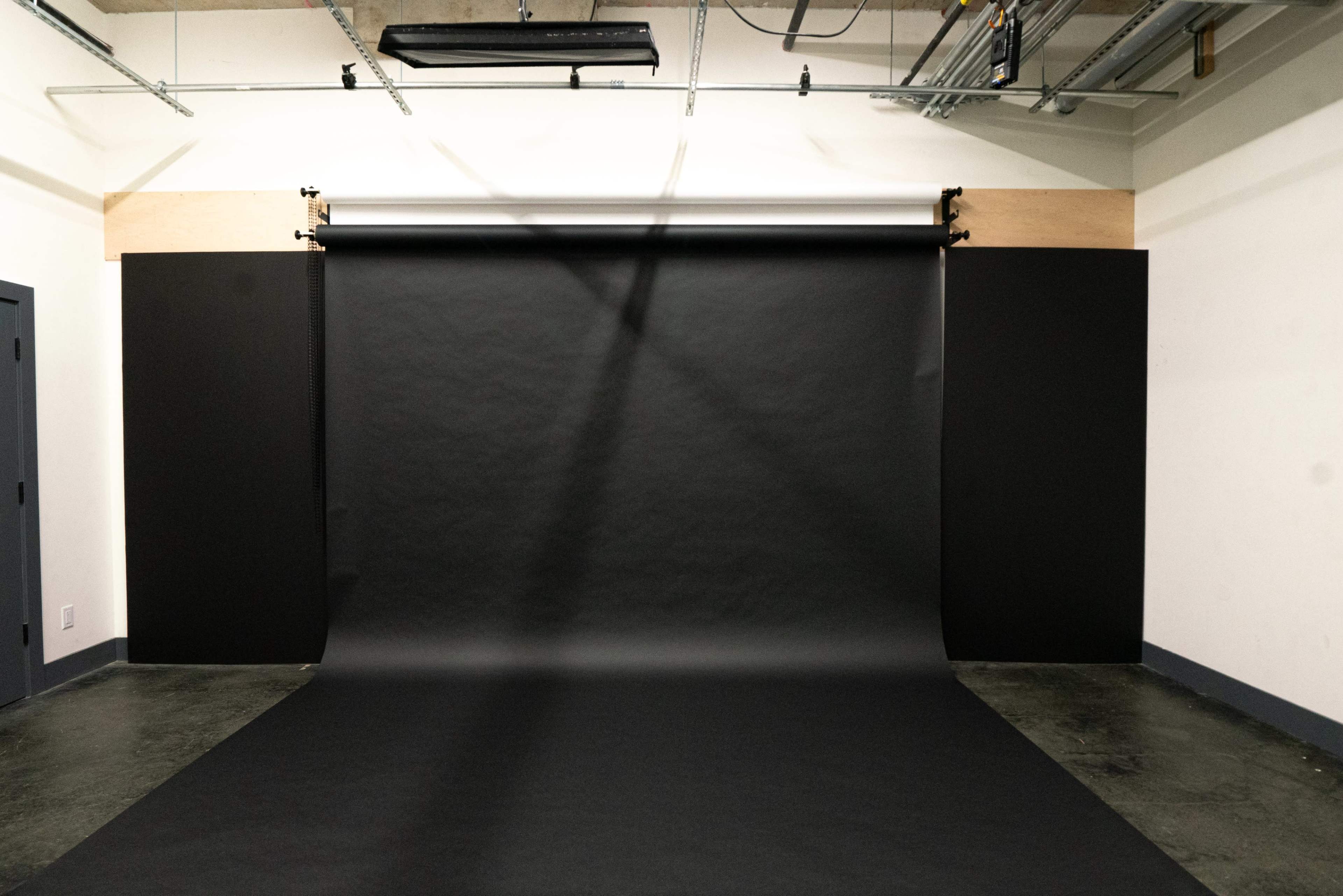 A photo studio with a black backdrop, including a roll of black paper and adjacent black walls, set against a clean, uncluttered space.