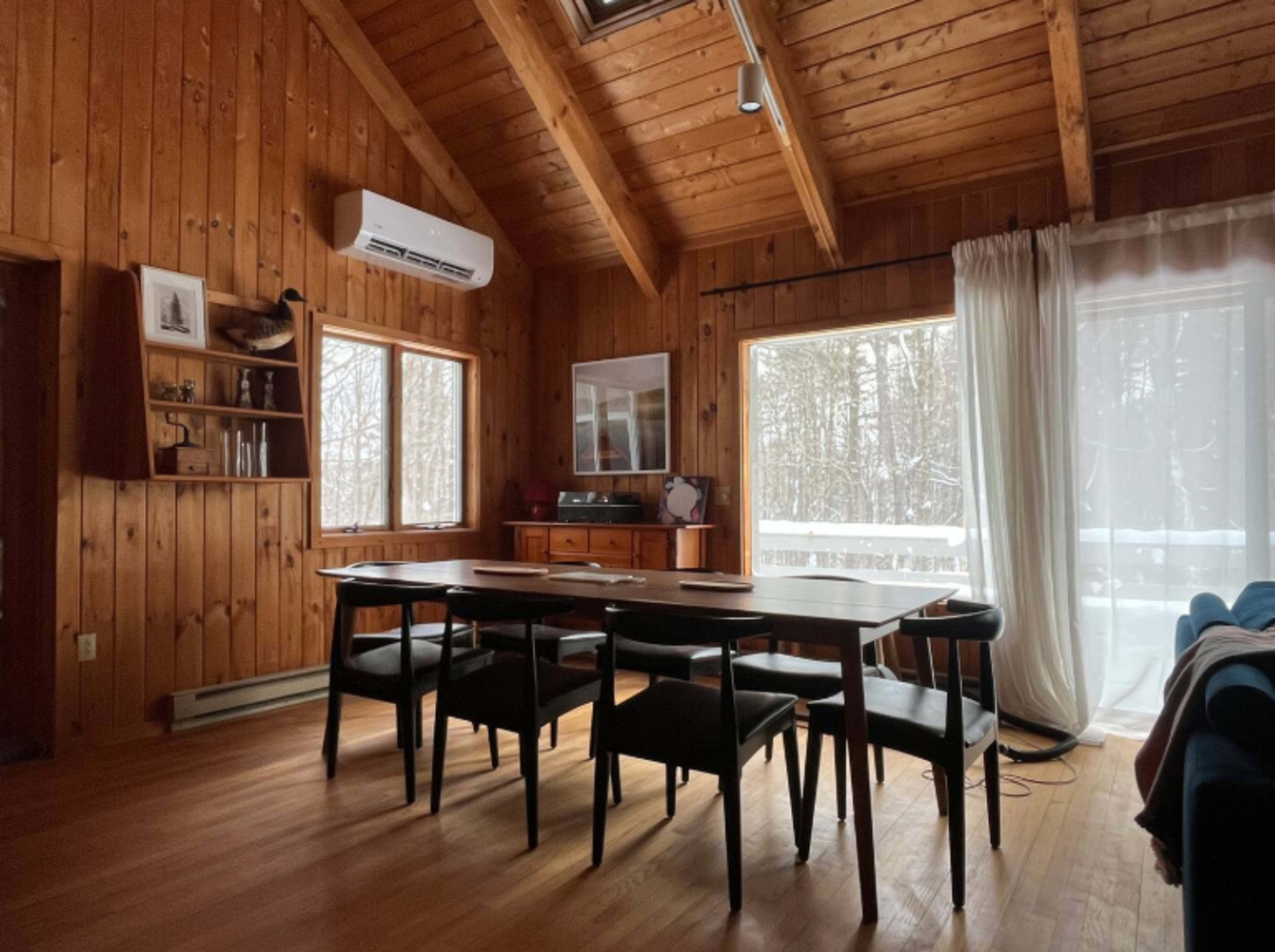 The image shows a wooden interior dining area with a large table, black chairs, and windows overlooking a snowy outdoor landscape.
