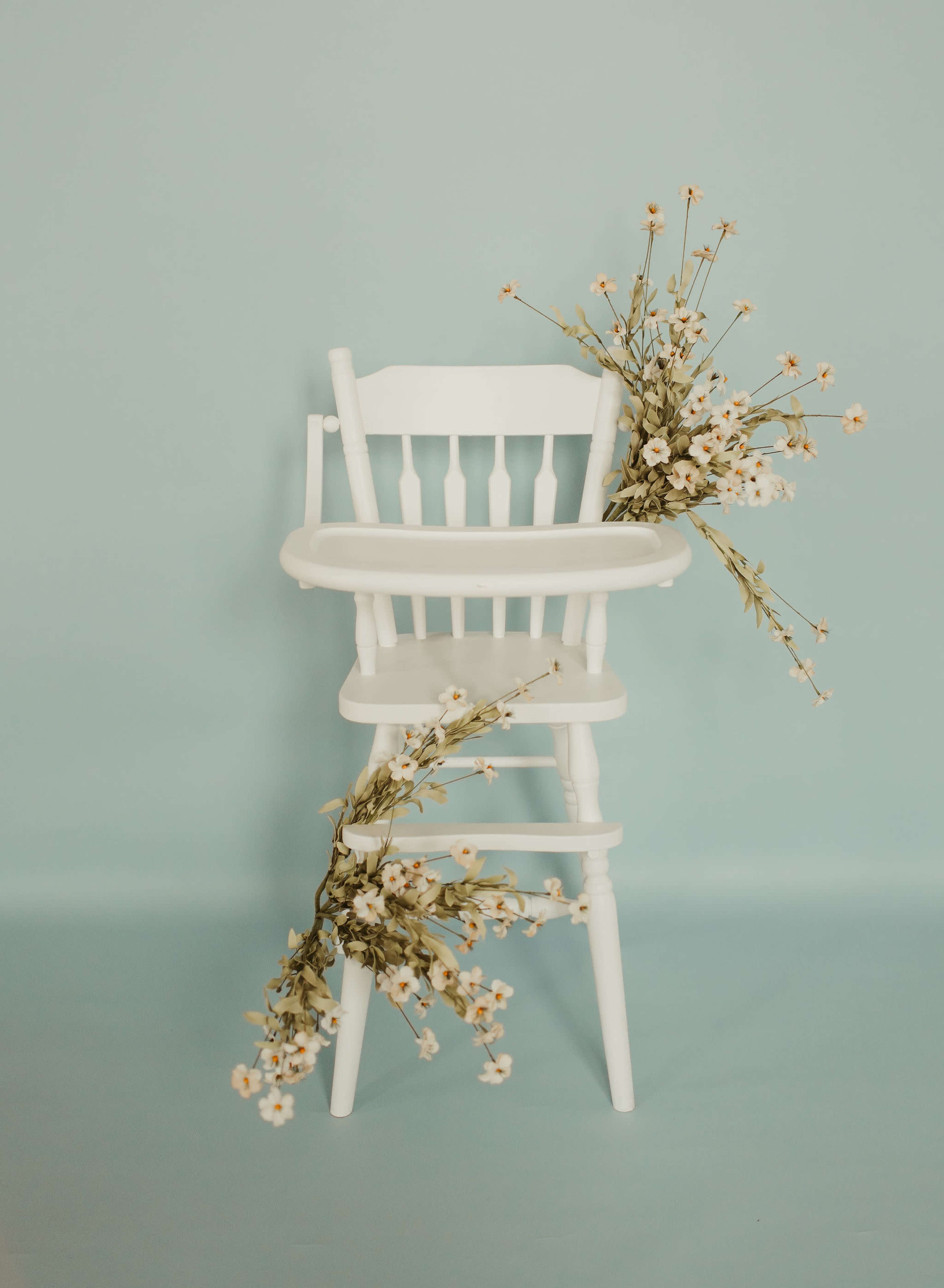 A white high chair is decorated with delicate flowers on a light blue background.