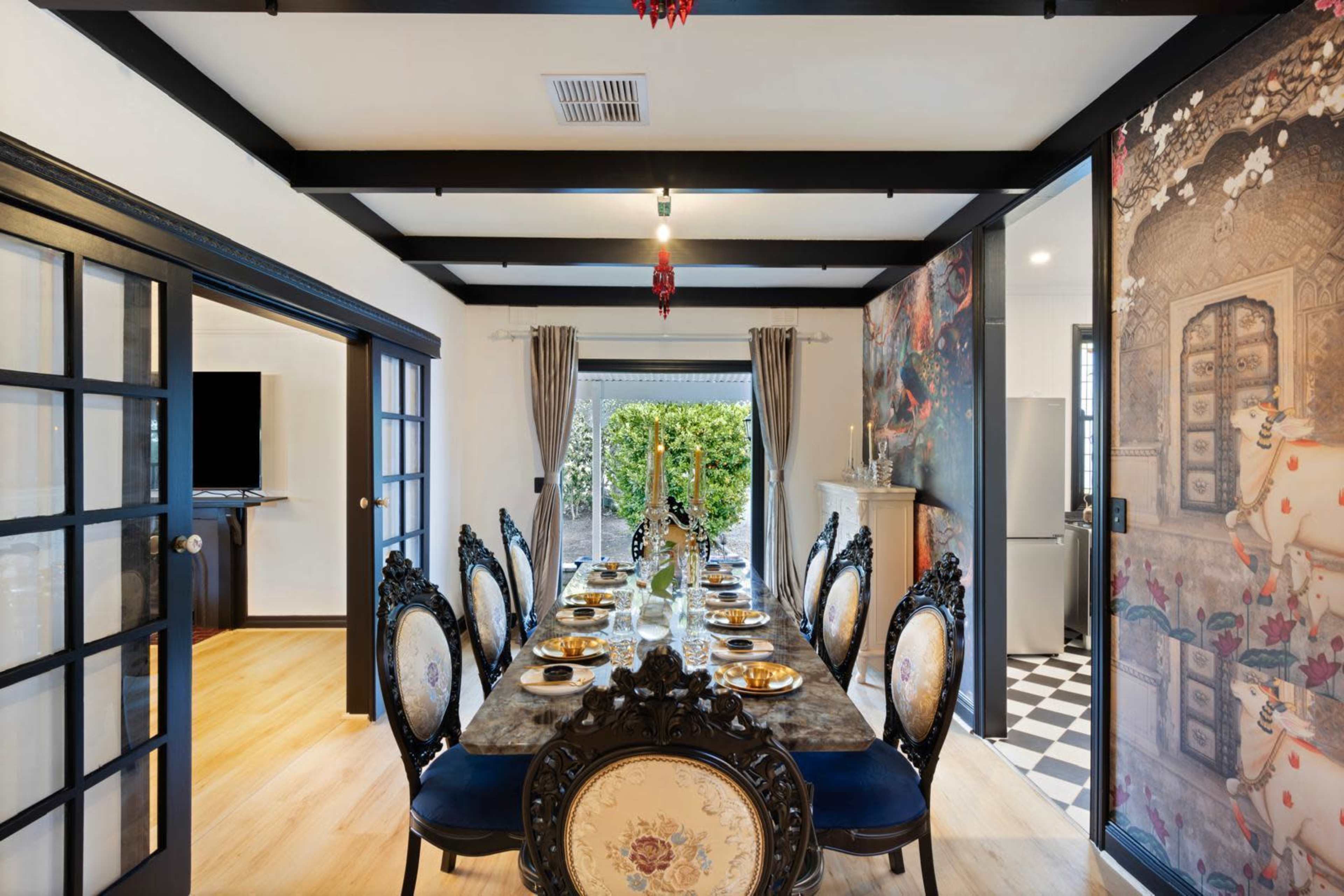 The image shows a formal dining room with a long table set for a meal, surrounded by ornate chairs and decorated with elegant tableware.