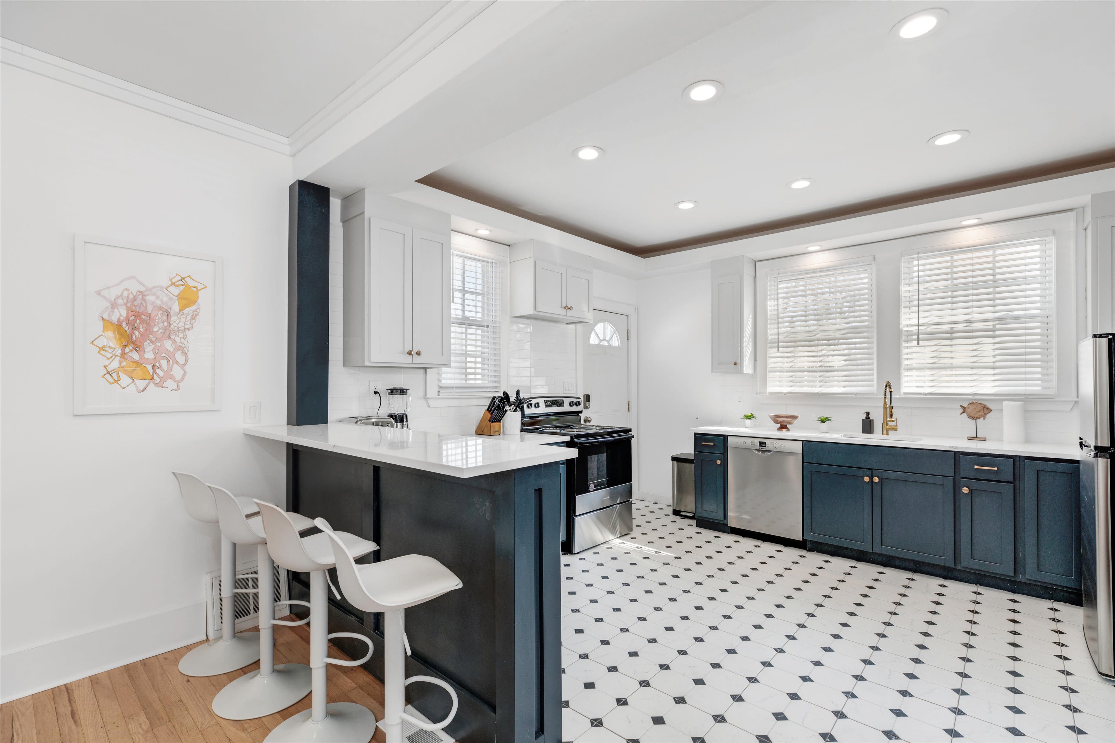 A modern kitchen features white cabinetry, dark blue lower cabinets, and a black stove, with a tiled floor and bar seating.