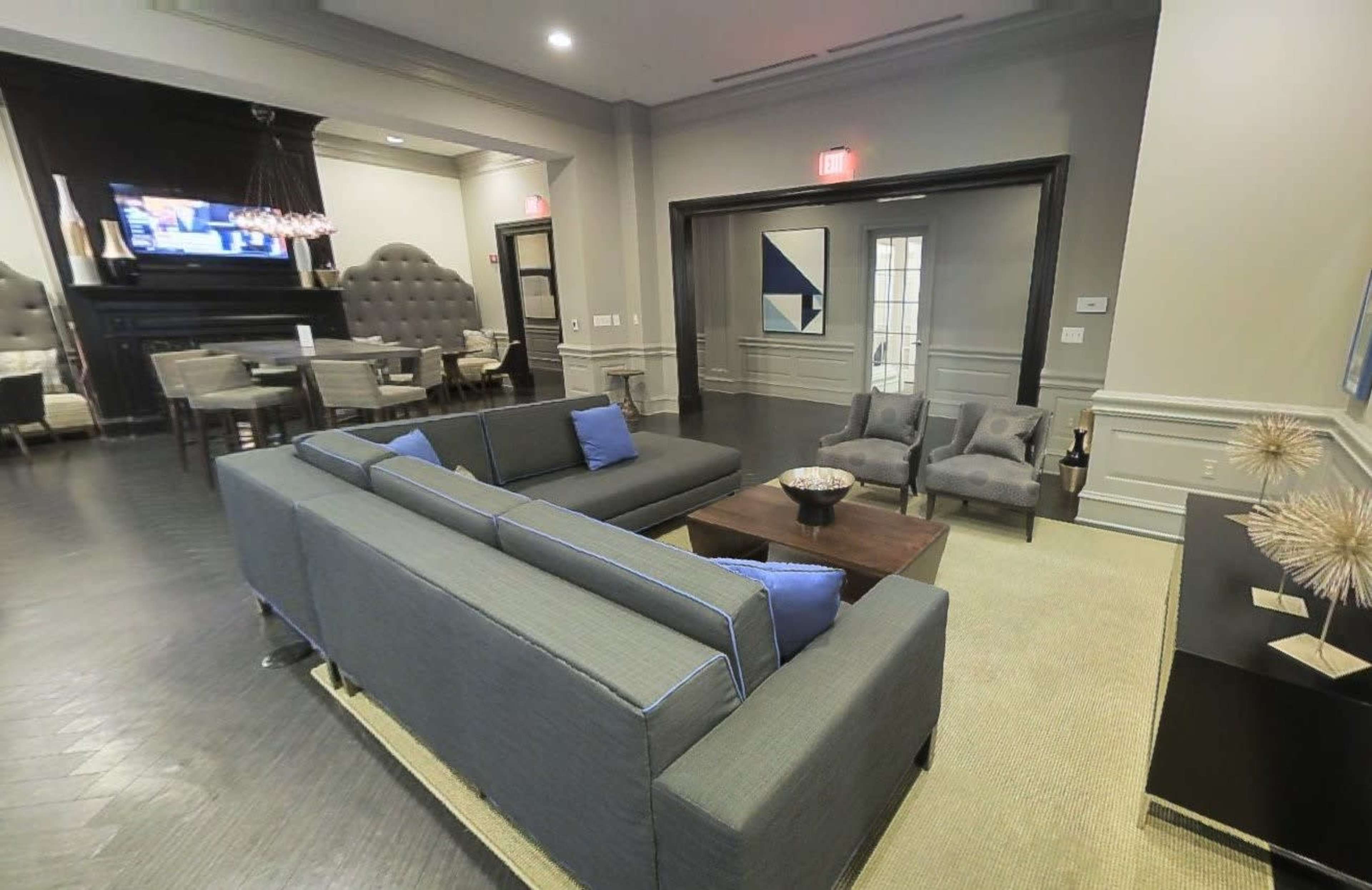 A modern lounge area featuring a gray sectional sofa with blue cushions, a dark wood coffee table, and a wall-mounted TV in a stylish interior.