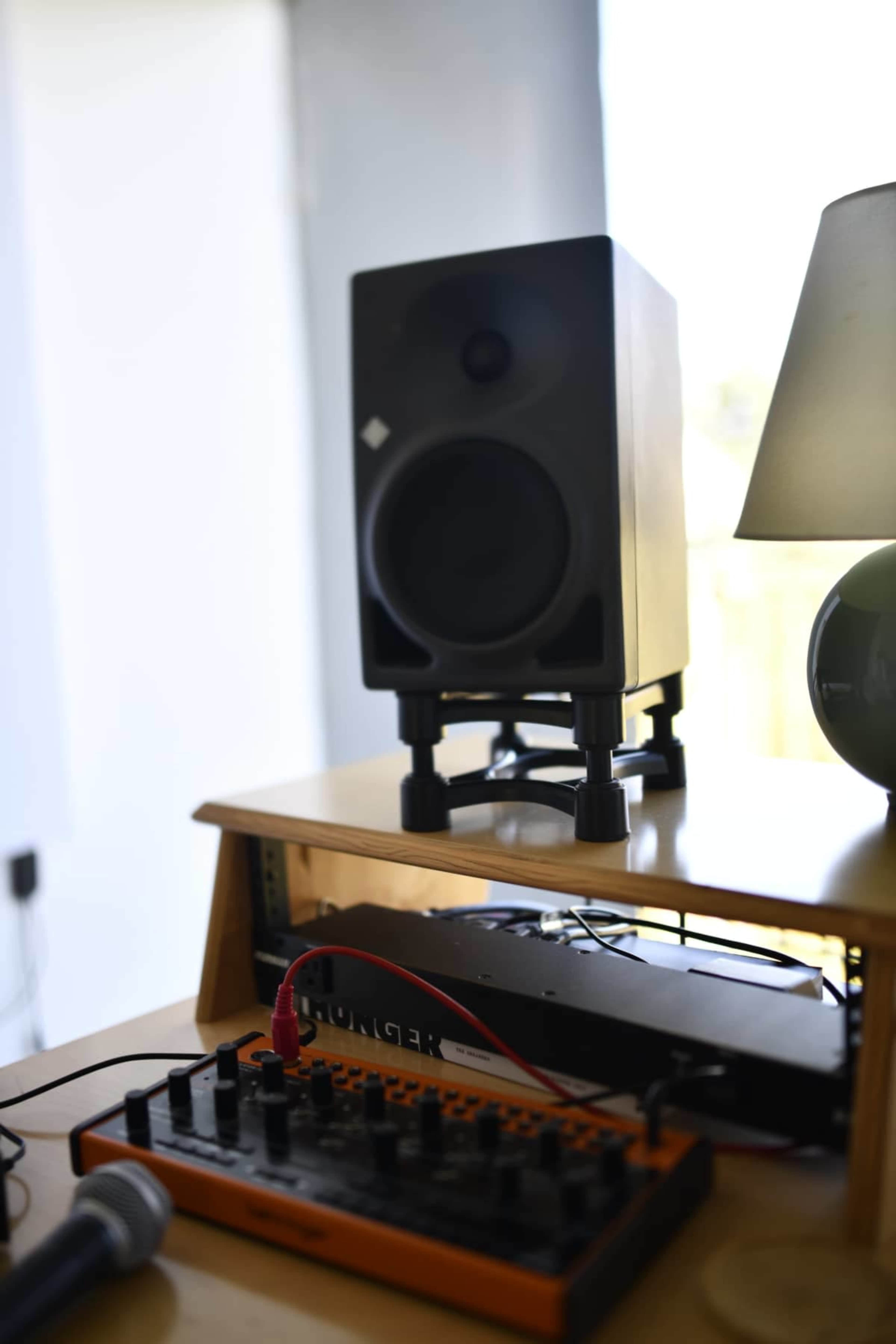 A black speaker sits on a wooden stand next to a microphone and a small electronic music device.