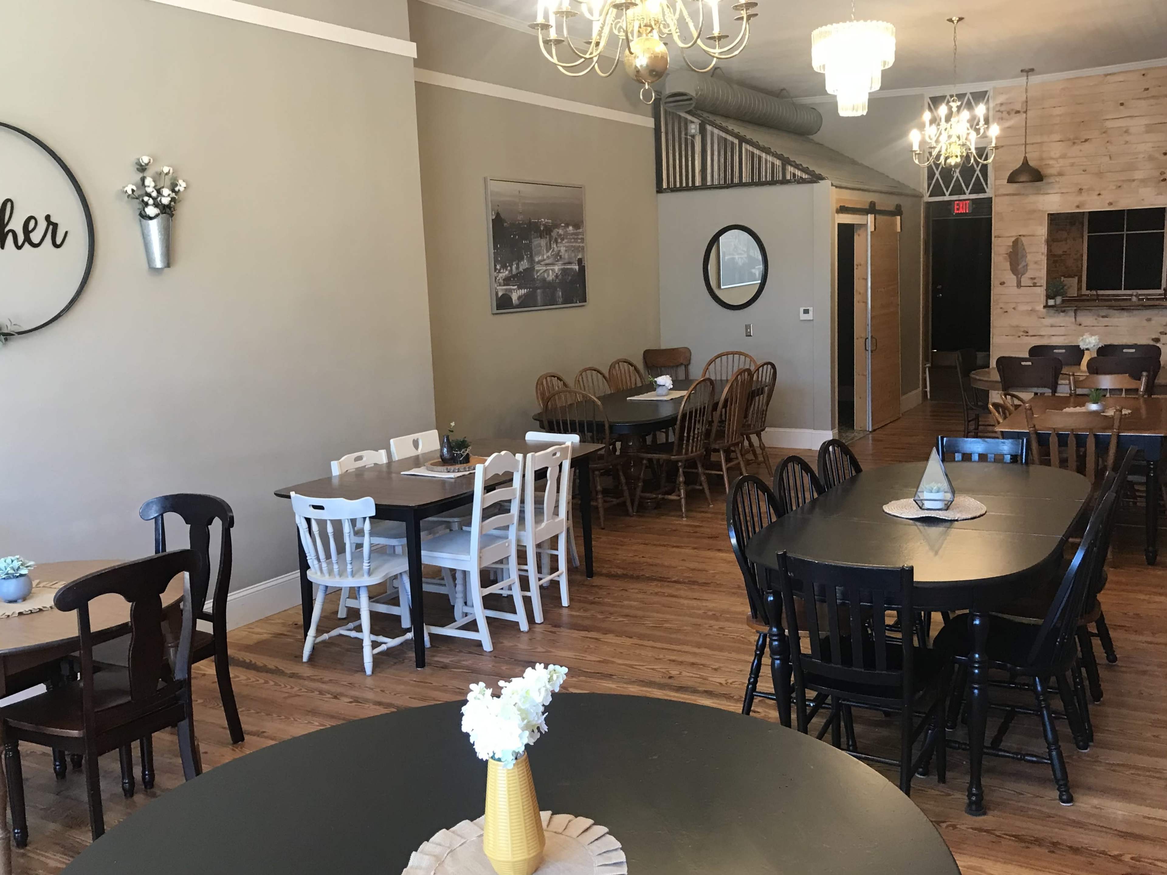 The image shows a spacious dining area with various tables and chairs arranged around the room, featuring a mix of light and dark wood finishes.