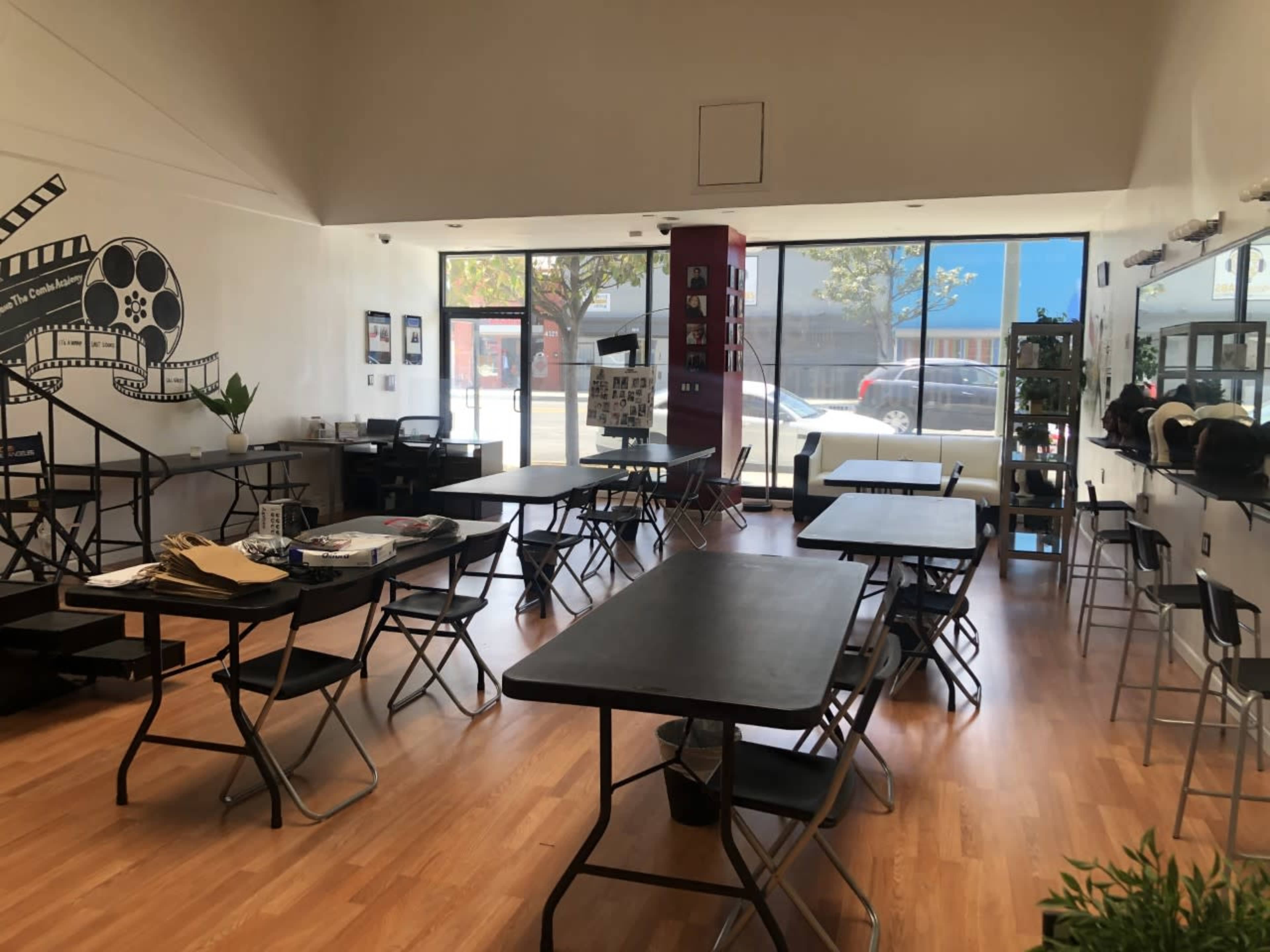 A well-lit studio space with several black tables and chairs arranged throughout, featuring large windows that provide a view of the outside.