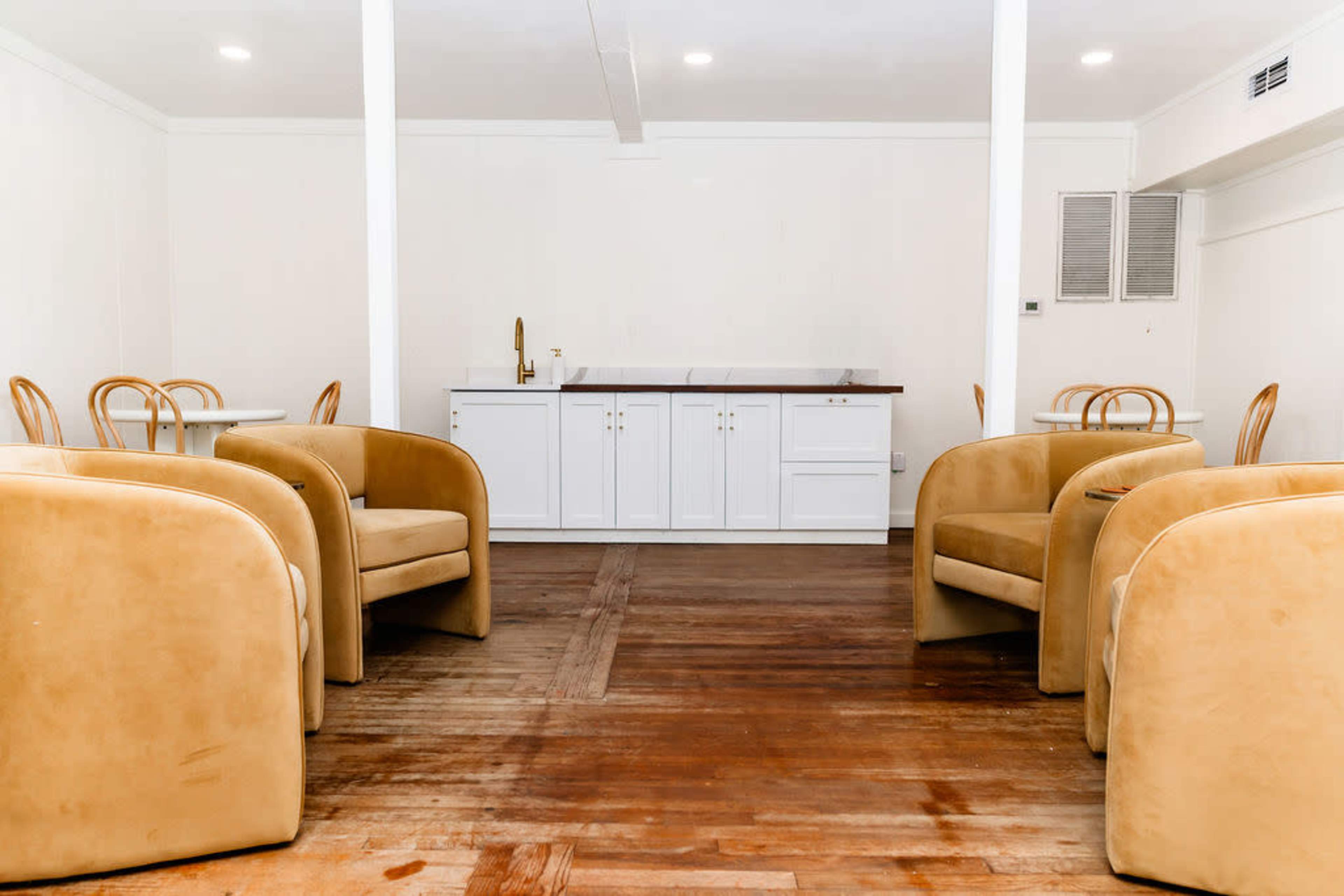 The image shows a spacious, minimalistic interior with four rounded chairs facing a bar-style counter against a plain wall.