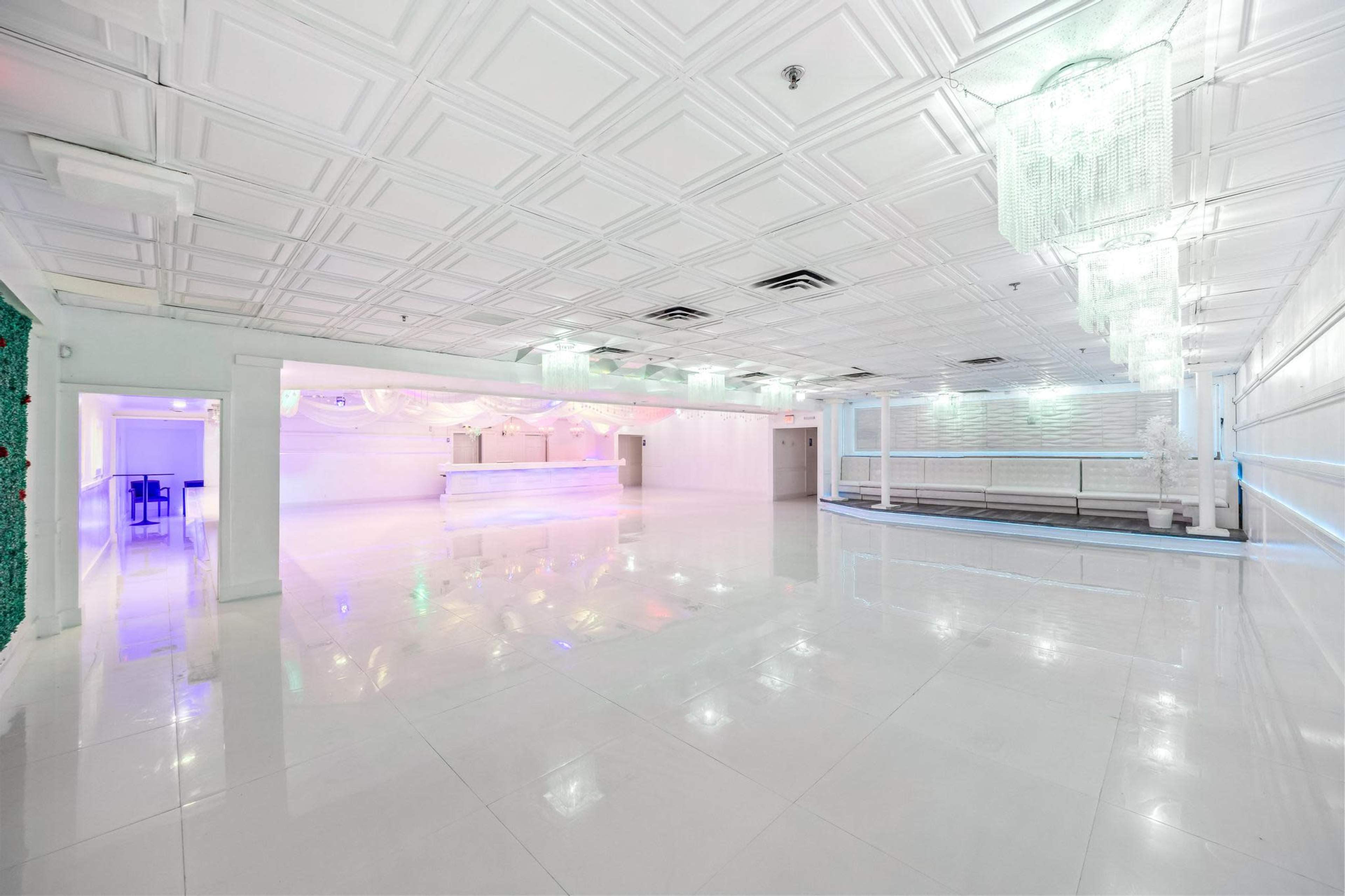 The image shows an empty, brightly lit event space with a glossy white floor and modern decor, including a bar area and decorative lighting.