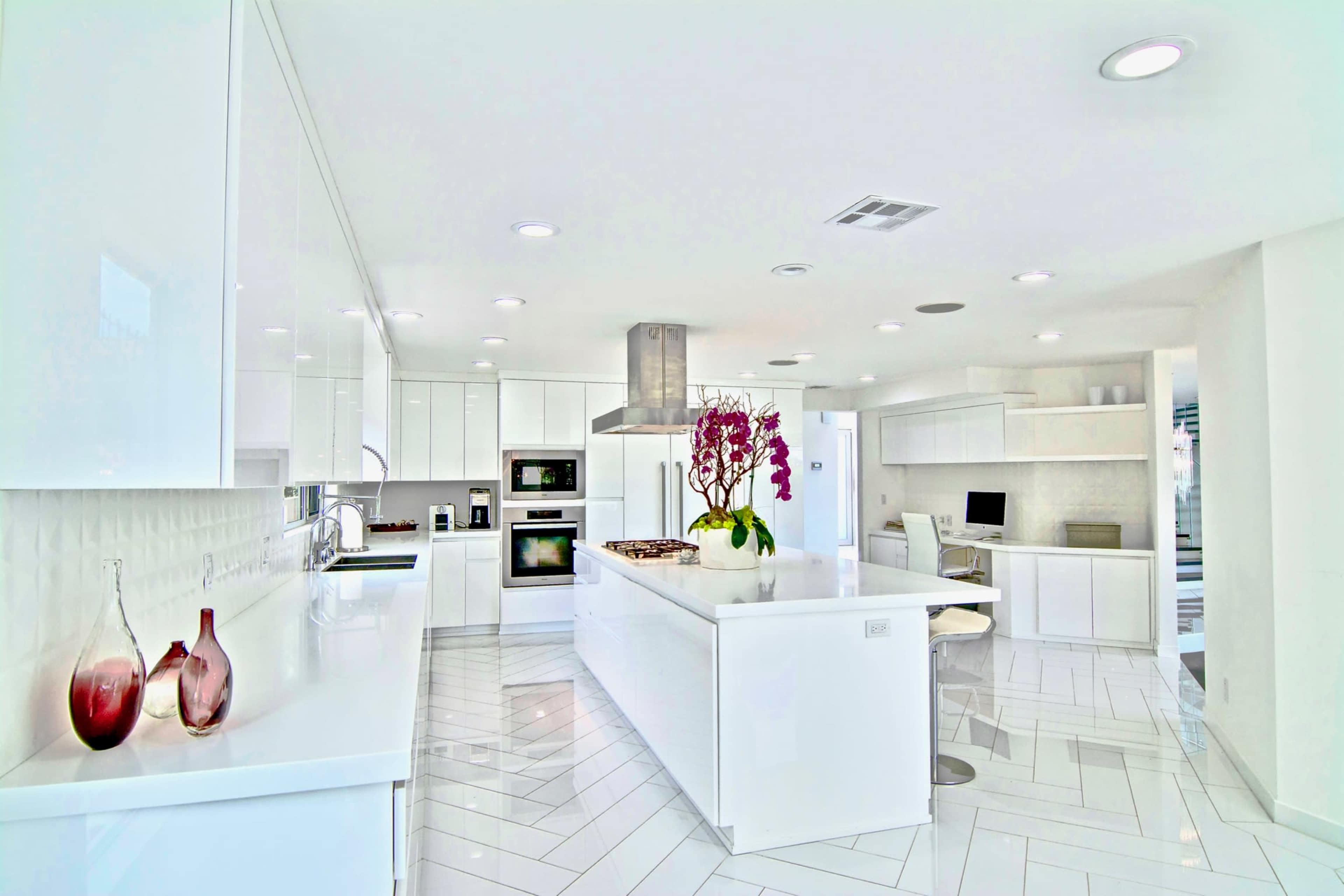 A modern kitchen features white cabinets, stainless steel appliances, and a large island with a vase of purple flowers.
