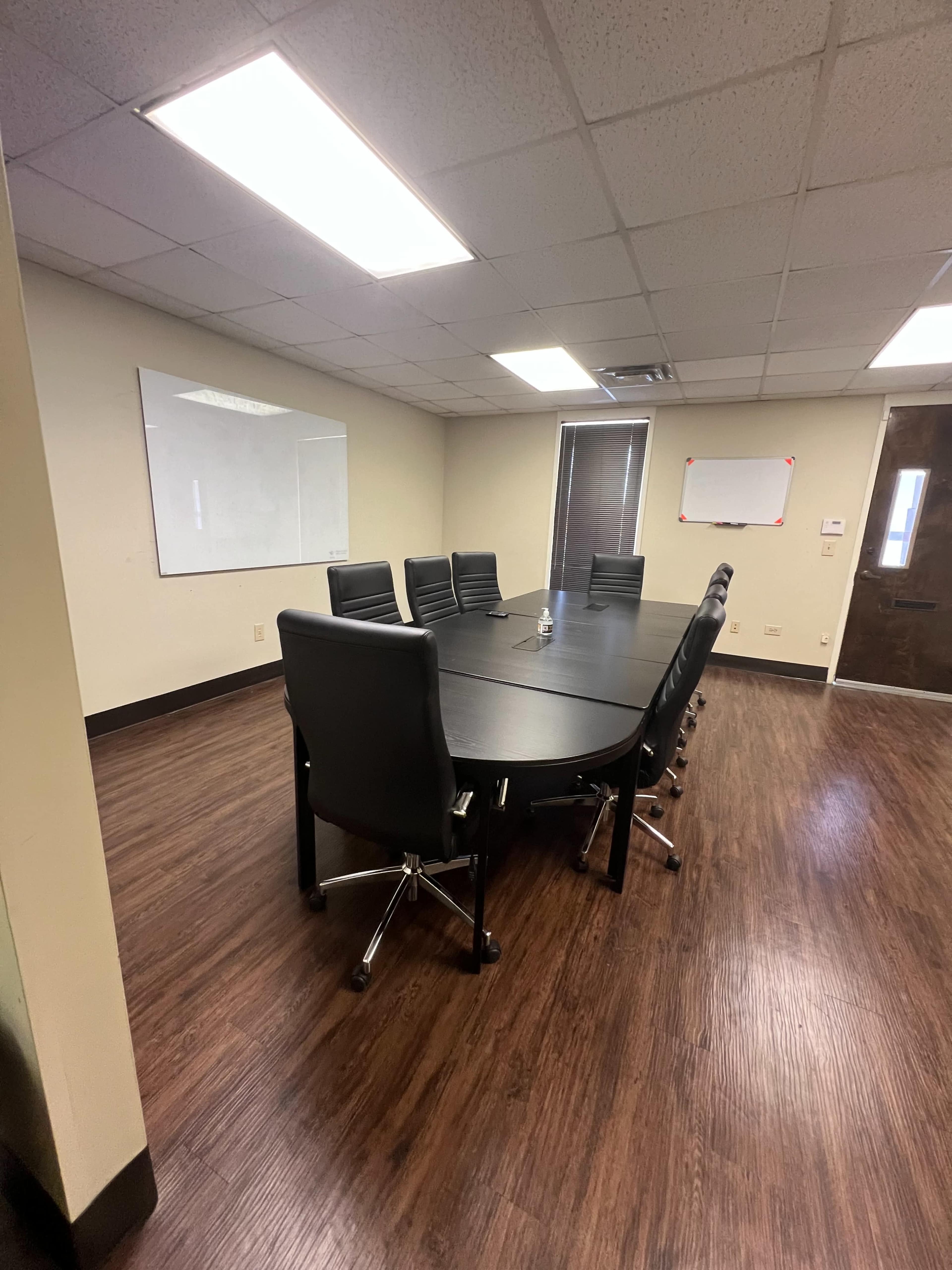 A conference room featuring a large circular table surrounded by black office chairs and whiteboards on the walls.